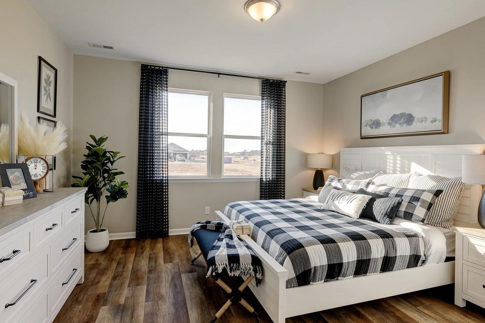 Spacious primary bedroom in Carroll Green, Harvest Alabama with checkered bedding, hardwood floors, and large windows