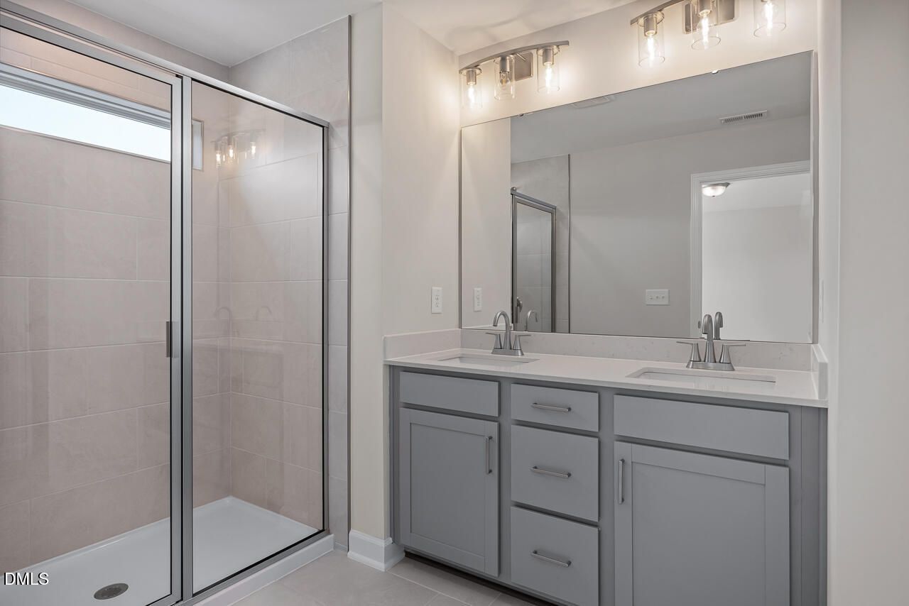Modern bathroom with dual vanity and glass-enclosed shower in The Mitchell floor plan at Camden Park, Knightdale, NC.