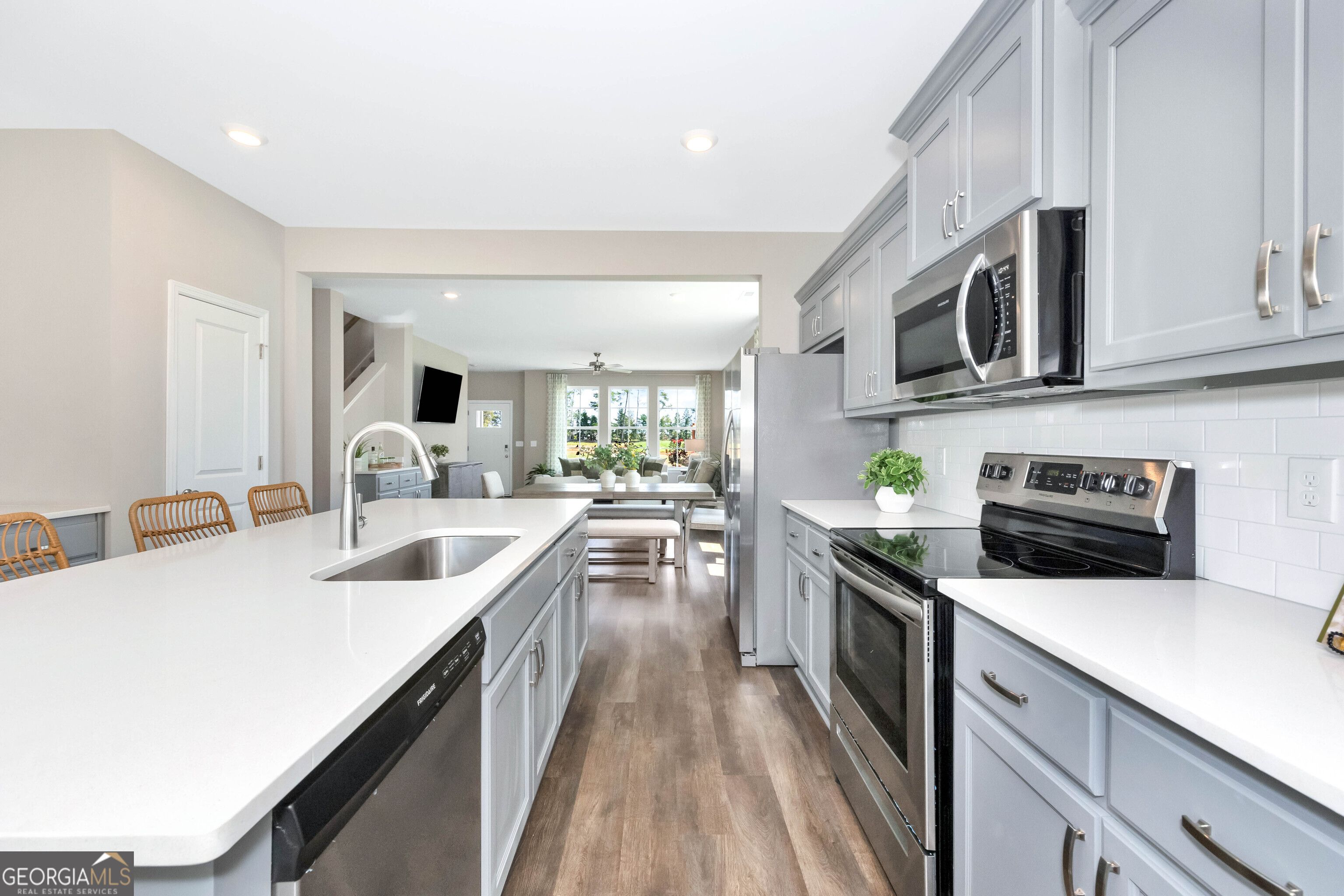 Modern open-concept kitchen with gray cabinets, white quartz counters, stainless appliances in Evermore Homes The Stella, Perry, GA