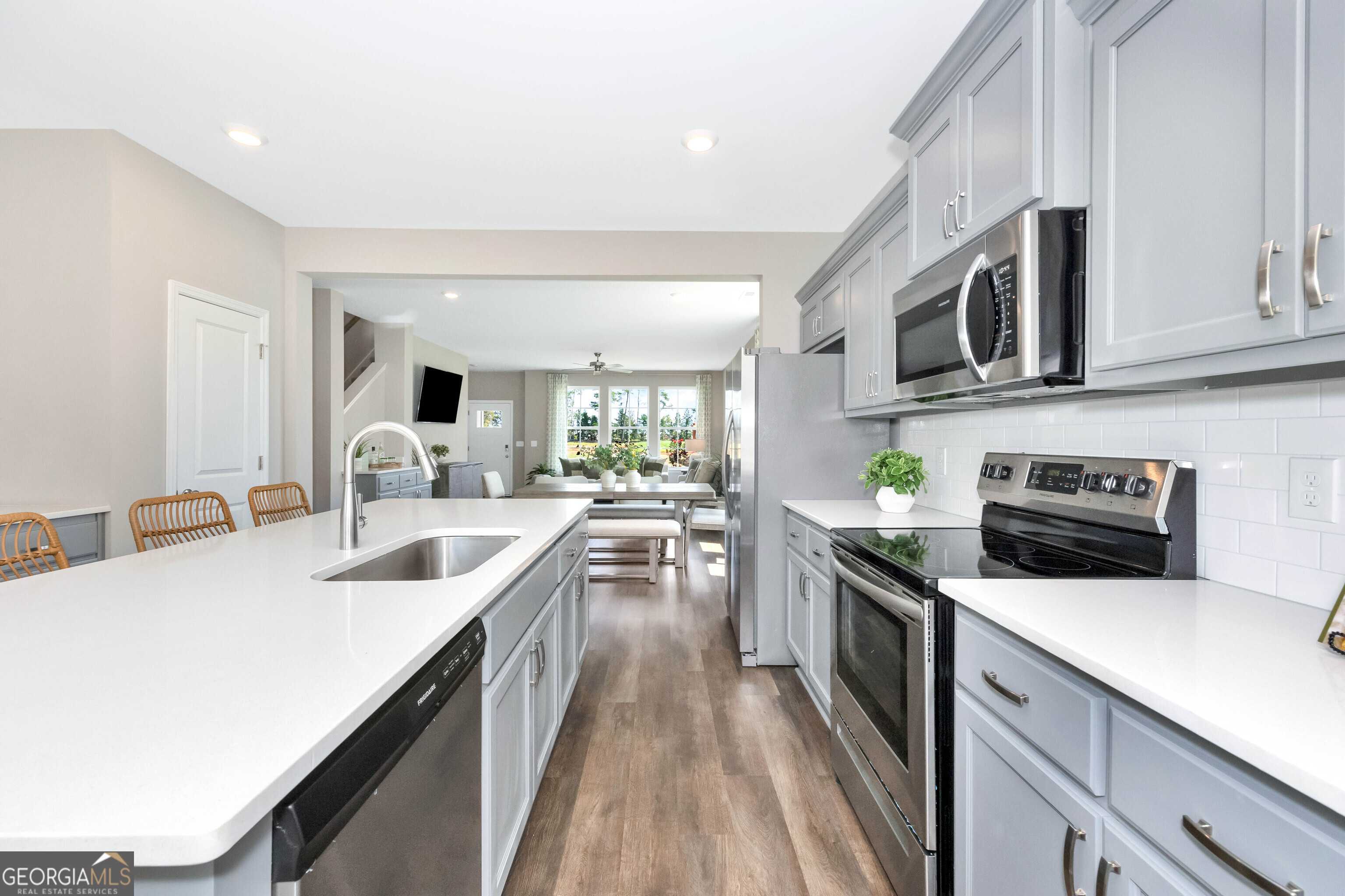 Modern open-concept kitchen with gray cabinets, white quartz counters, stainless appliances in Evermore Homes The Stella, Perry, GA