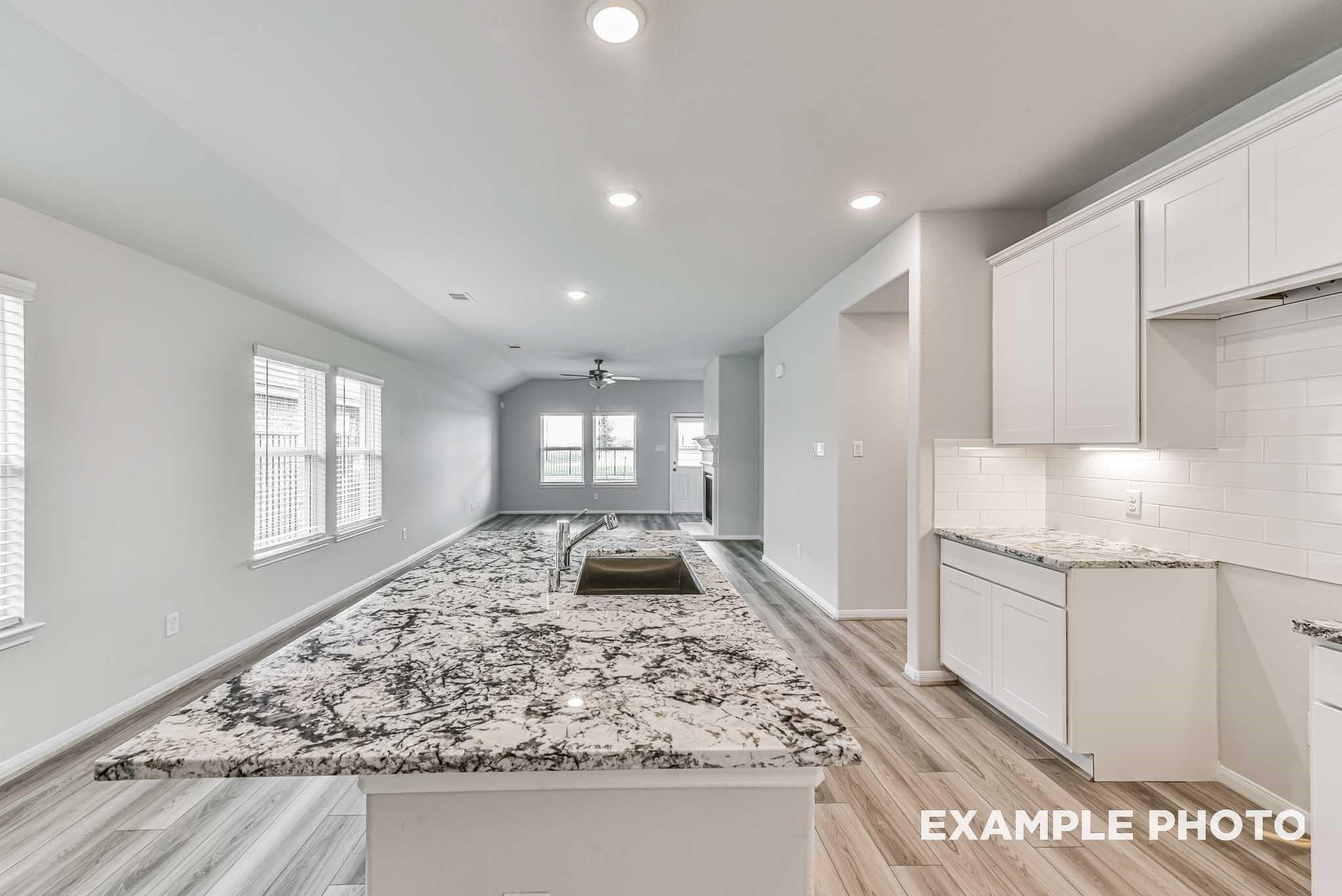 Open-concept kitchen with speckled granite island, white shaker cabinets, and subway tile backsplash in The Riviera A, Rosharon, Texas