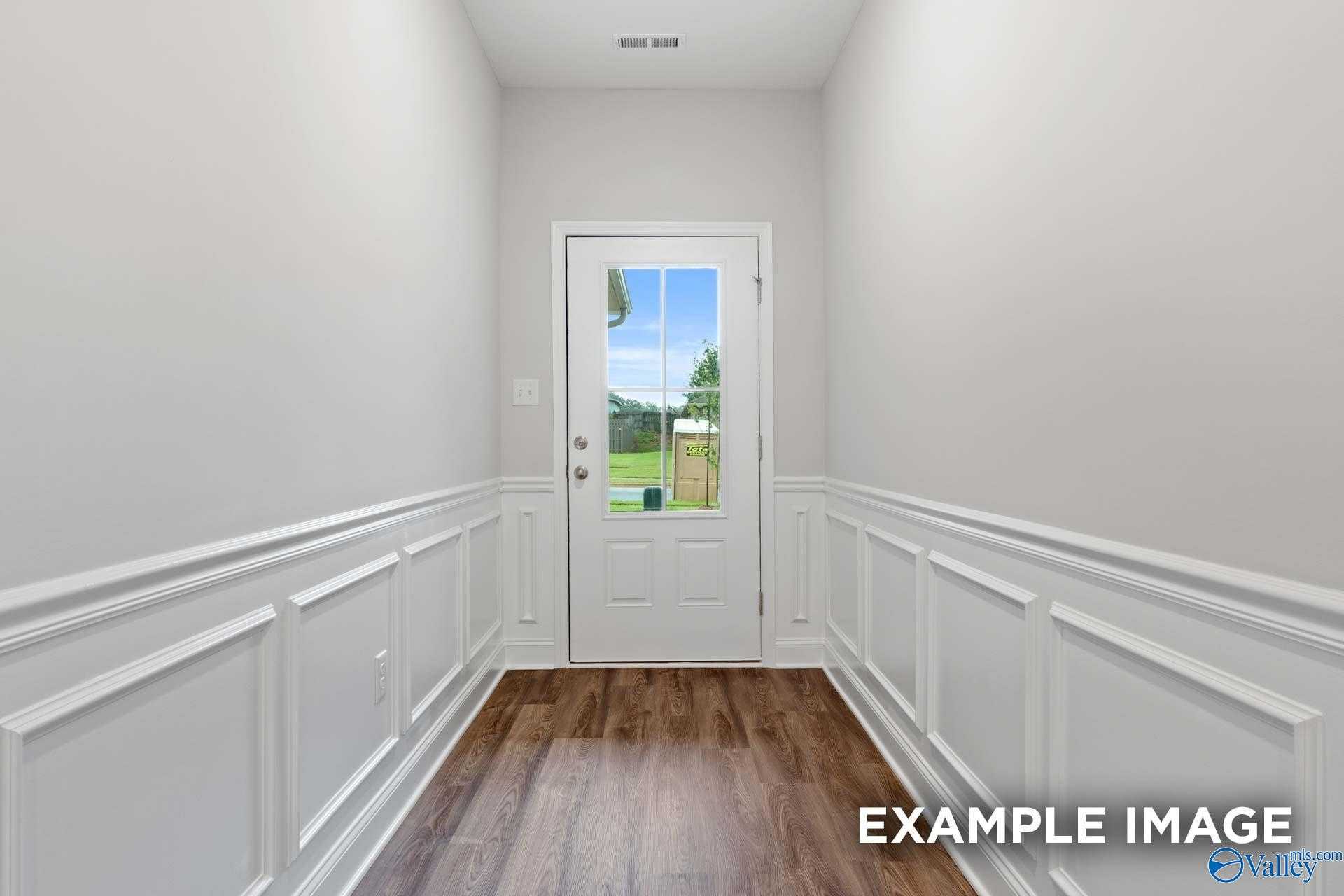 Elegant hallway with white wainscoting walls and hardwood floors leading to glass-paneled door in Davidson Homes The Cumberland, Decatur, AL