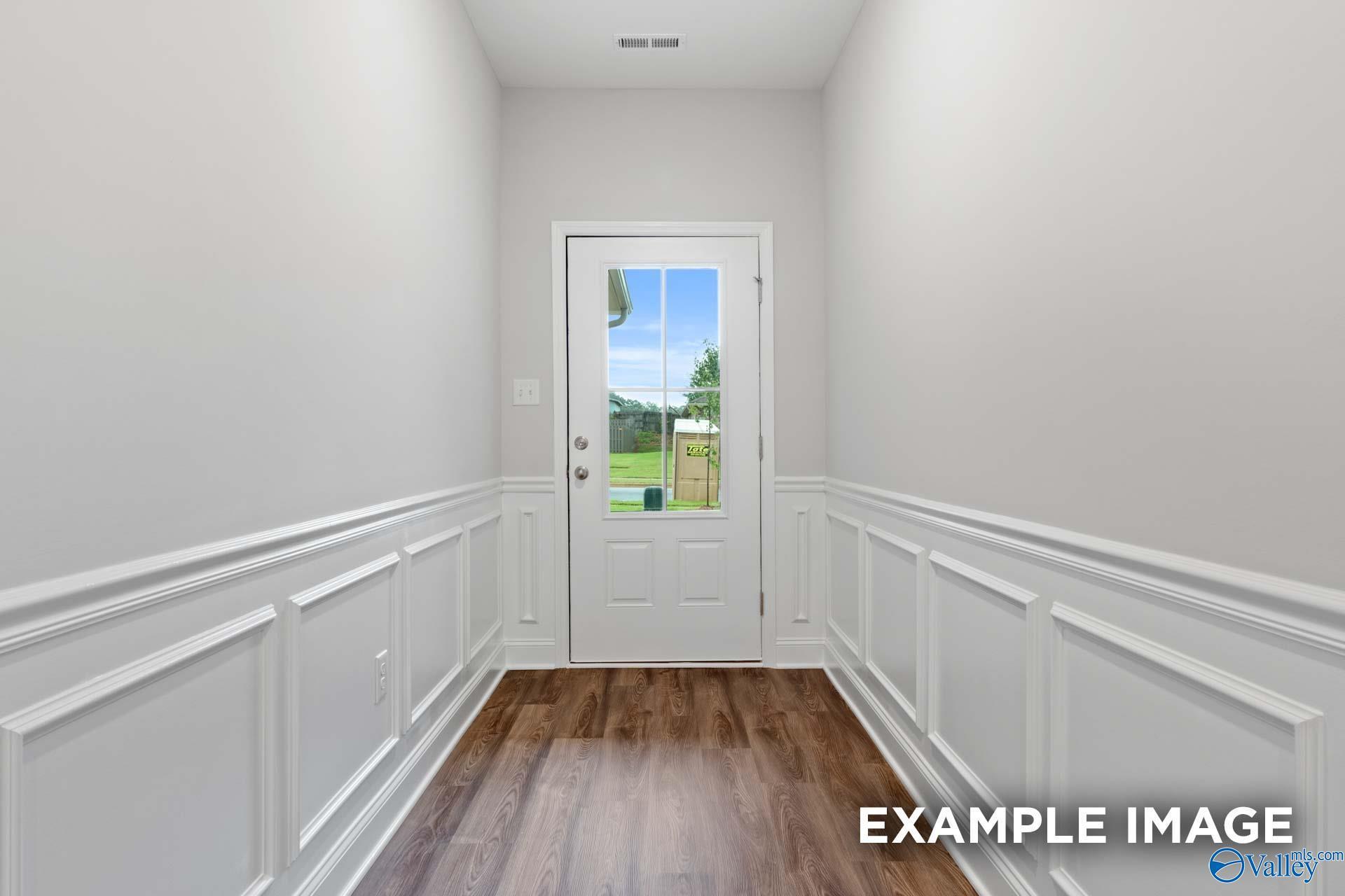 Elegant hallway with white wainscoting, hardwood floors, and glass-paneled door overlooking green yard in Davidson Homes The Cumberland, Decatur, Alabama