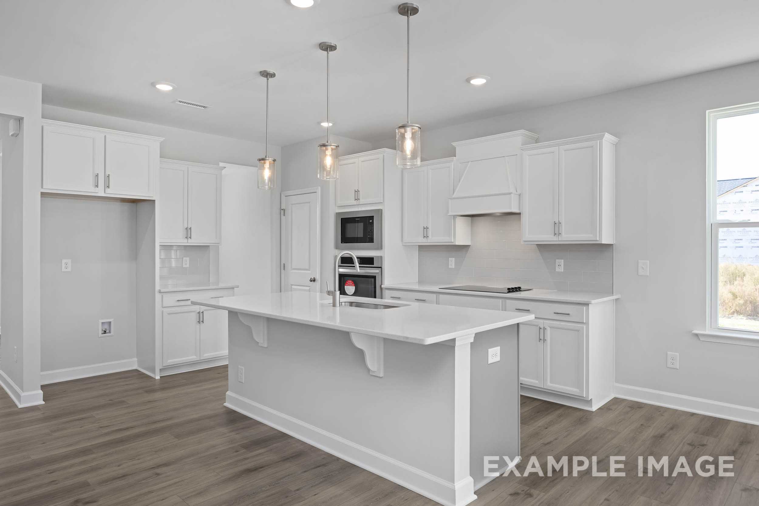 Spacious white kitchen in The Ash by Davidson Homes featuring large island, stainless appliances, and pendant lights