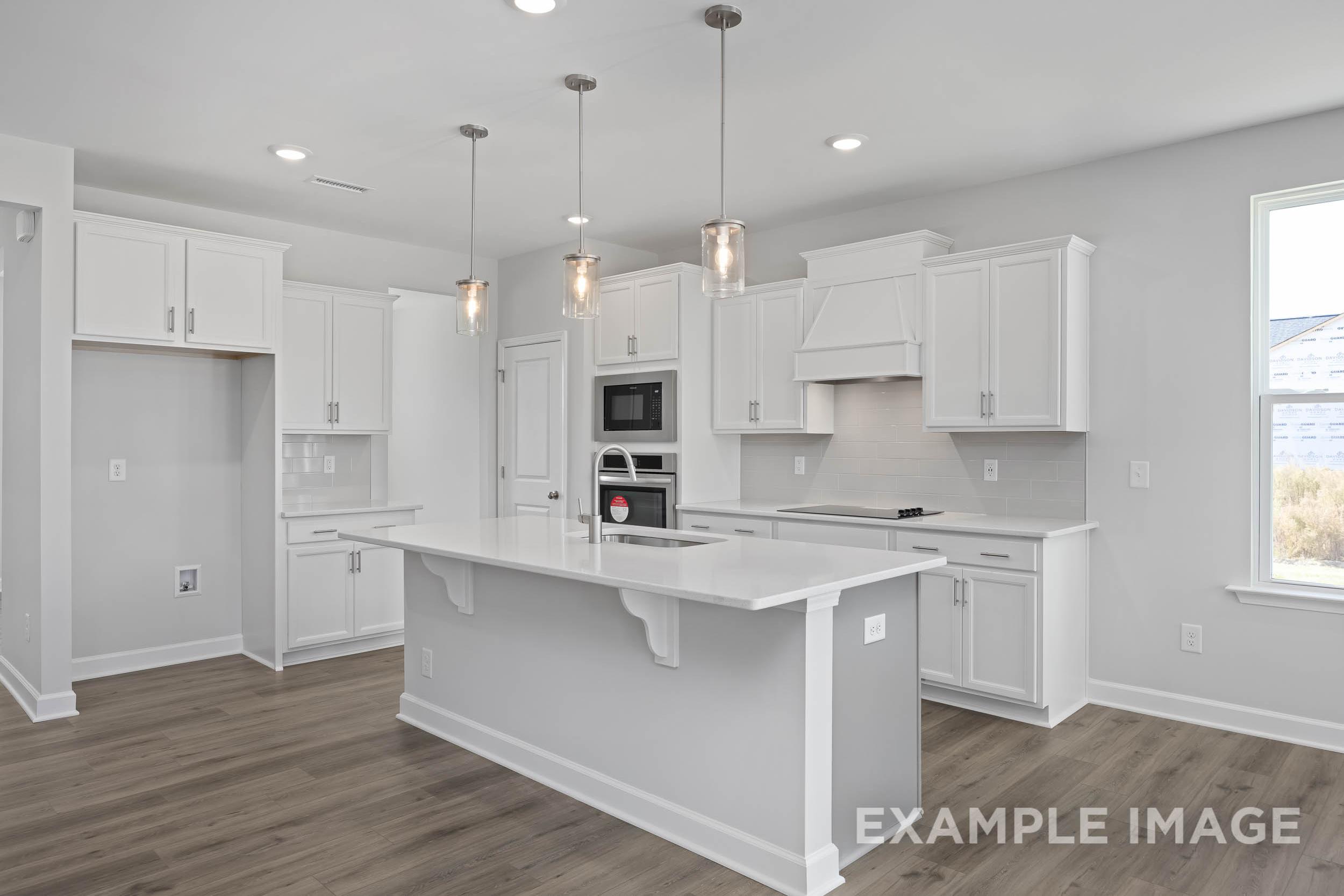 Spacious white kitchen in The Ash by Davidson Homes featuring large island, stainless appliances, and pendant lights