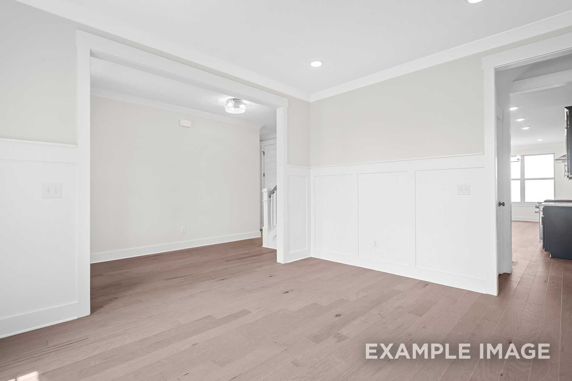 Spacious foyer in The Hawkins two-story home with white wainscoting, open archways, staircase, and hardwood floors