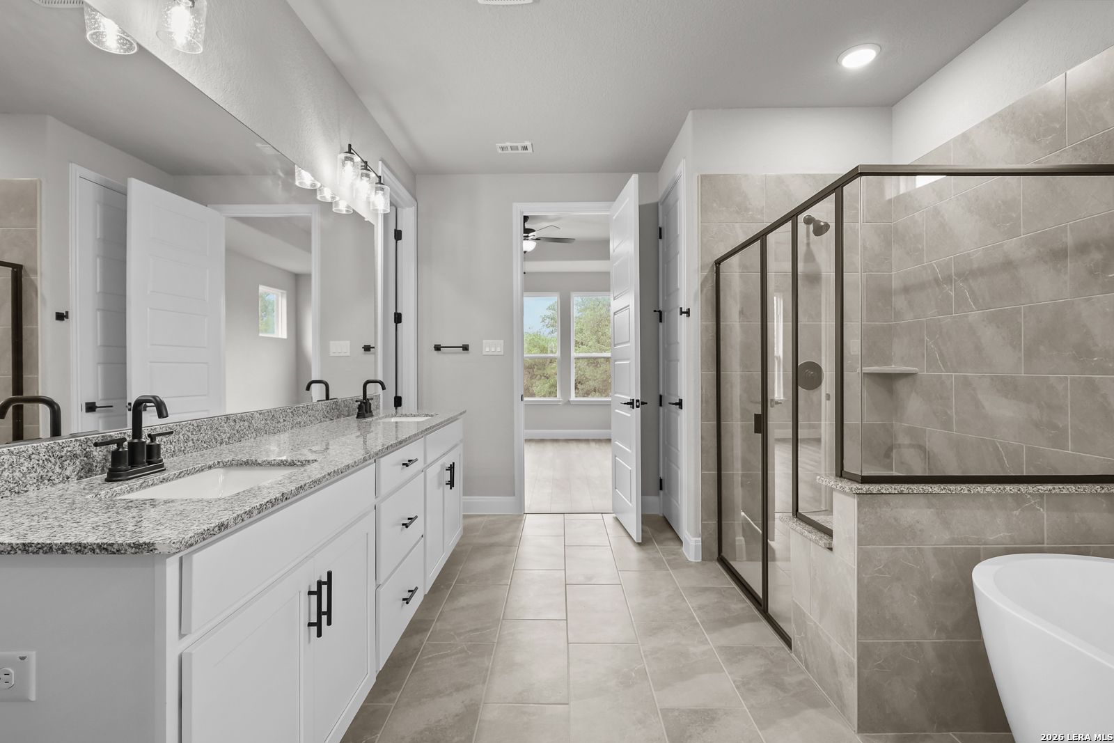 Elegant master bathroom featuring double granite vanity, frameless glass shower, and freestanding tub in Davidson Homes The Belmont H, Castroville, Texas