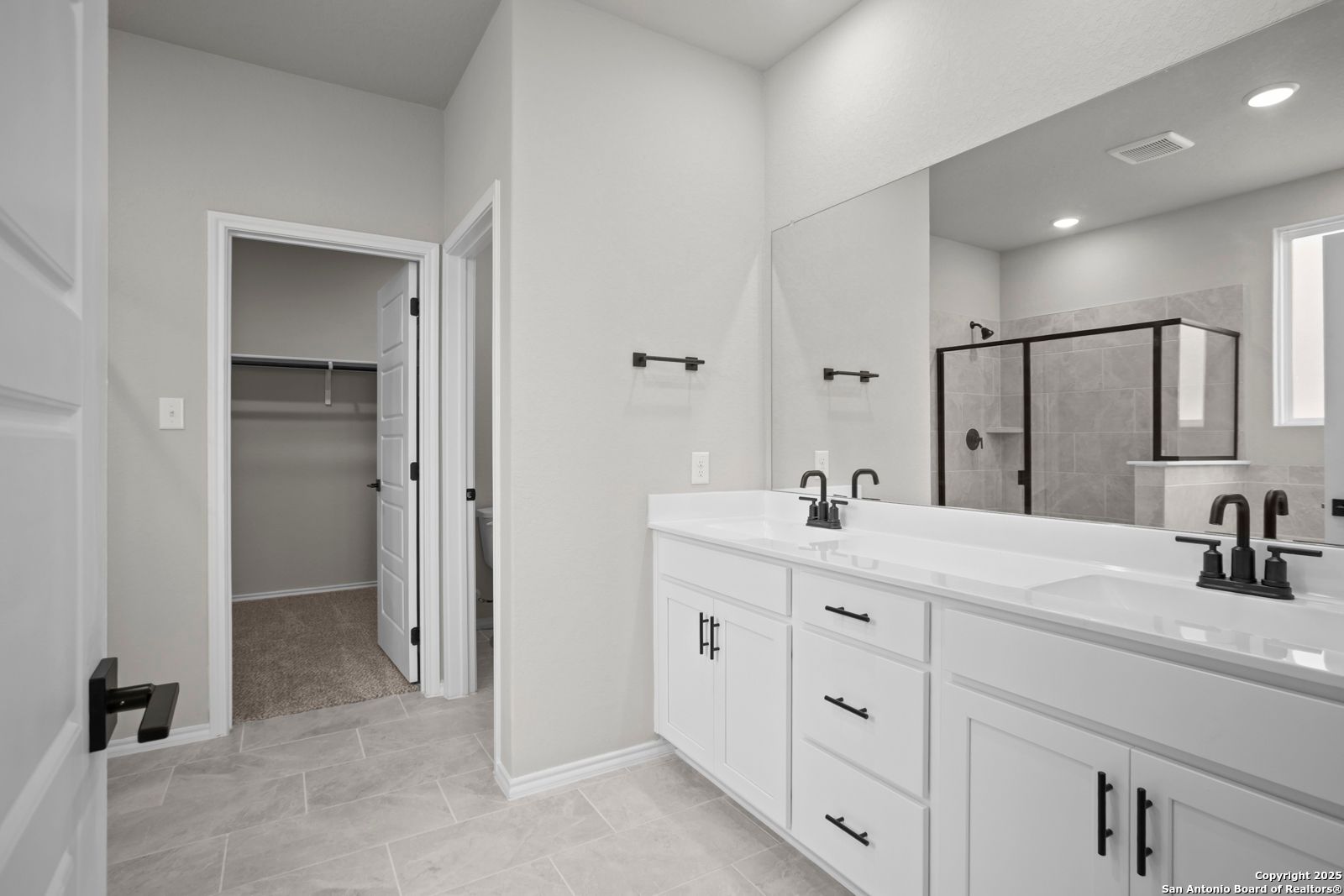 Modern master bathroom with double vanity, frameless glass shower, and walk-in closet in Davidson Homes The Sequoia A, Converse, TX