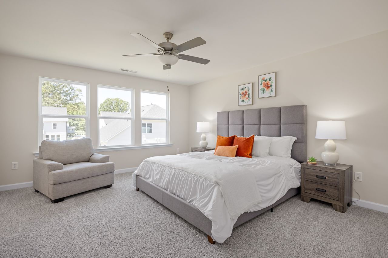 Spacious master bedroom in The Chestnut featuring a tufted headboard, cozy seating area, and large windows.