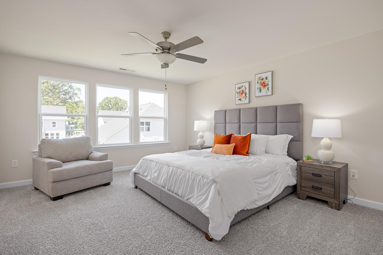 Spacious master bedroom in The Chestnut featuring a tufted headboard, cozy seating area, and large windows.