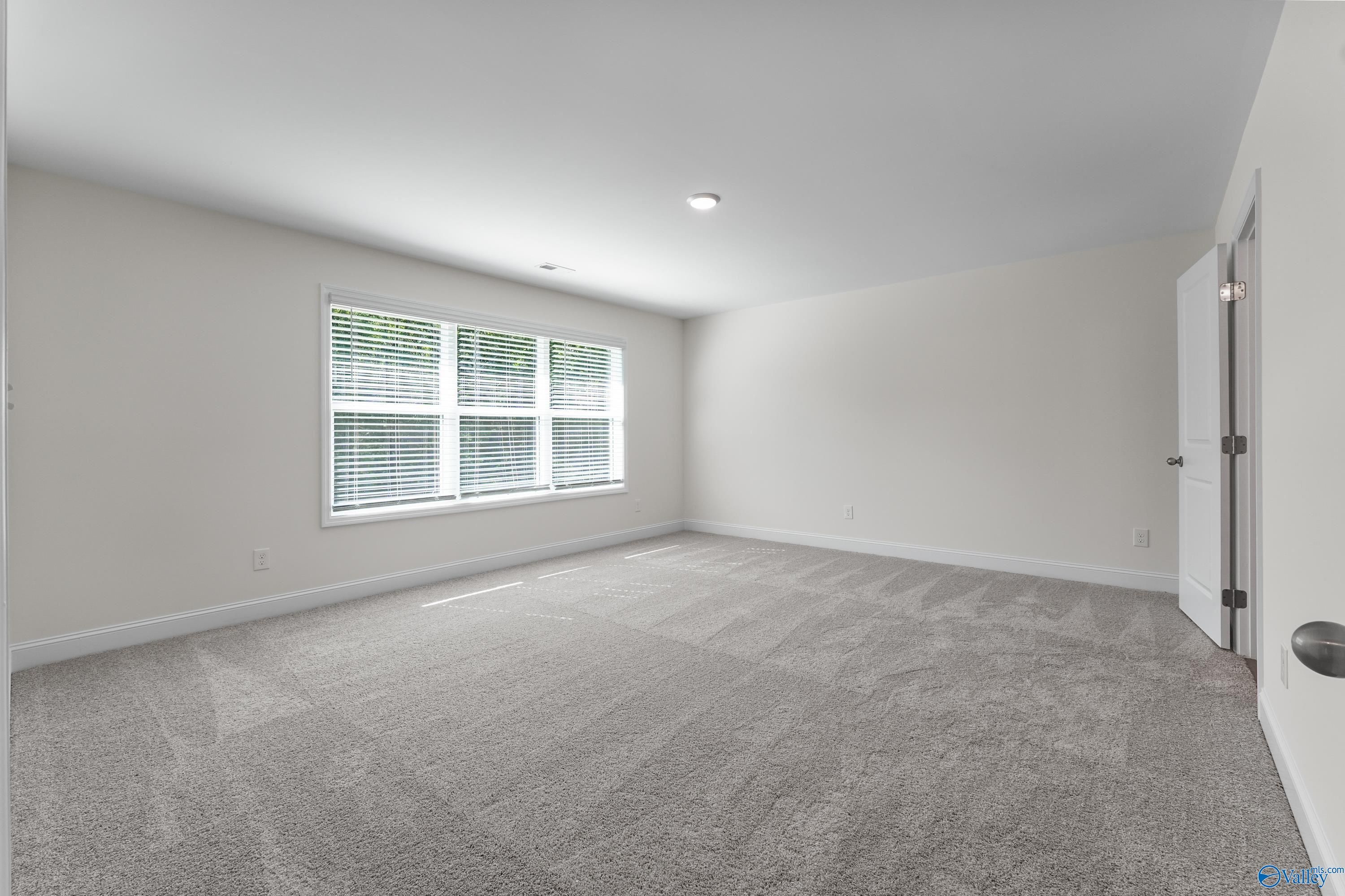 Spacious empty bedroom with triple windows, beige walls, and gray carpet in Davidson Homes Shelby A, Athens, Alabama