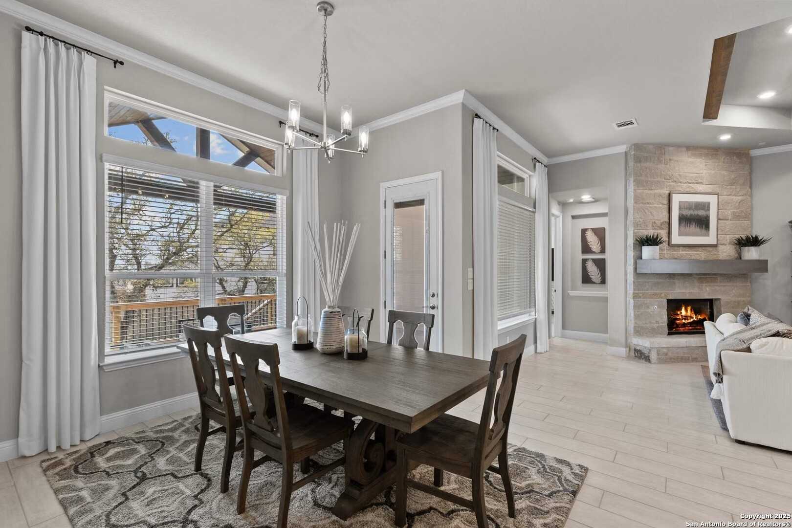 Elegant dining room with wooden table, chairs, and chandelier opening to living area with stone fireplace in Davidson Homes The Garner A, Castroville, Texas