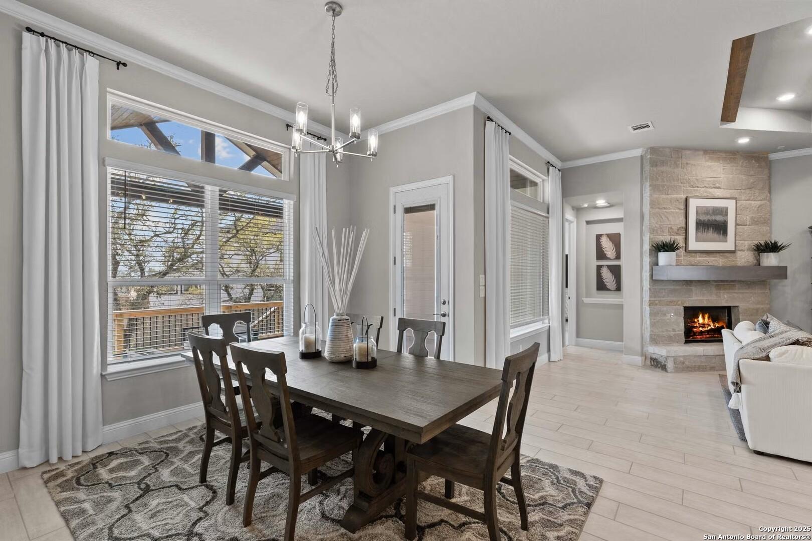Elegant dining room with wooden table, chandelier, large windows, open to fireplace living area in Davidson Homes The Garner B, Castroville, Texas