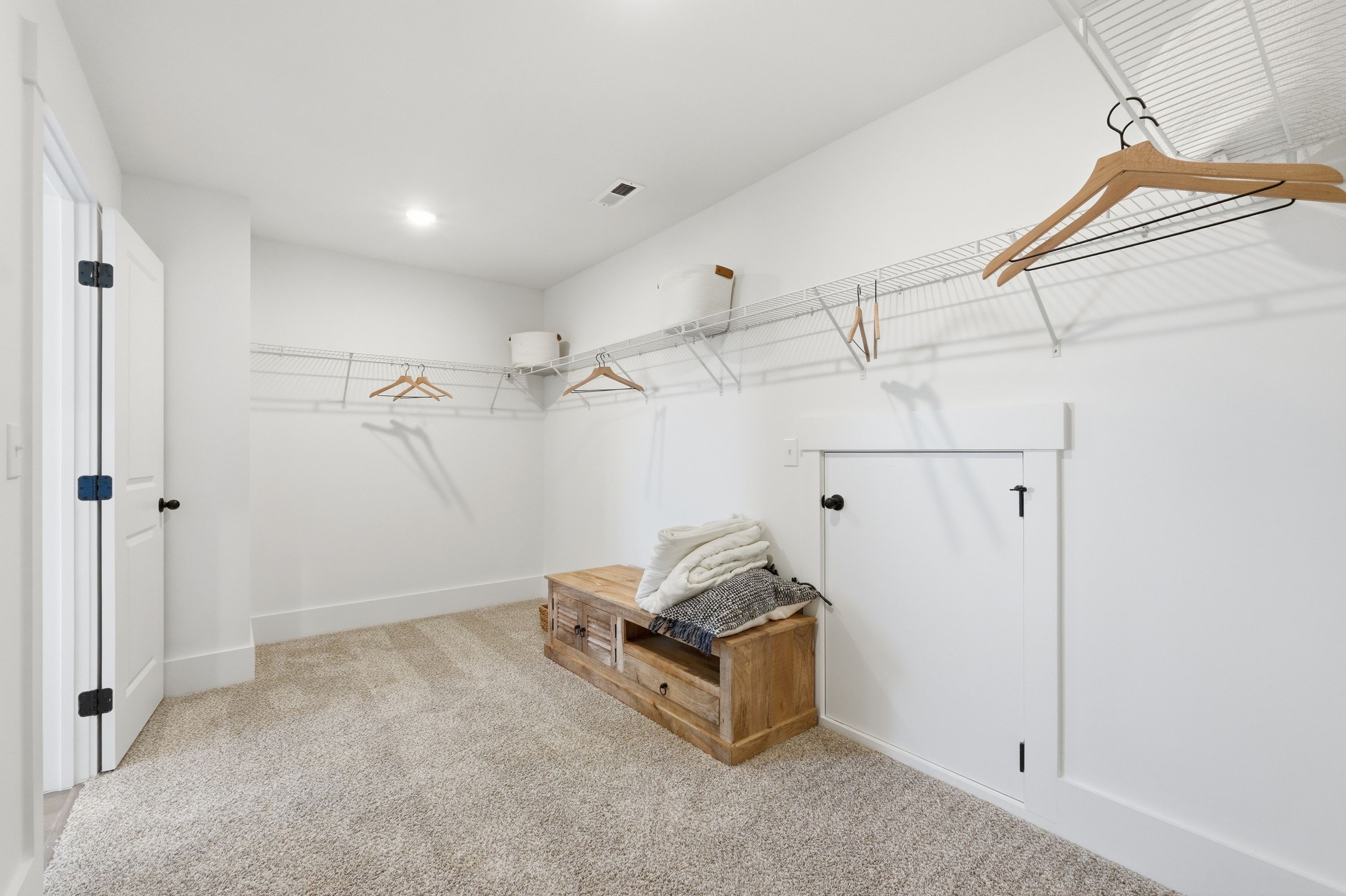 Spacious walk-in closet in Berry Cove home, New Market Alabama with white shiplap walls, wooden shelving, hanging rods, and built-in bench