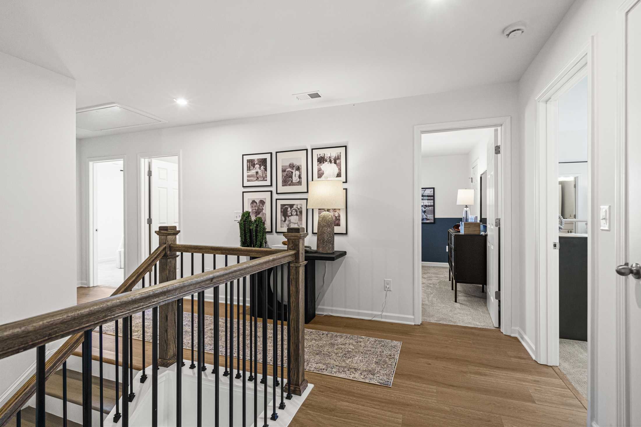 Spacious upstairs hallway in The Hickory A featuring wooden staircase with iron balusters, console table, and framed photos