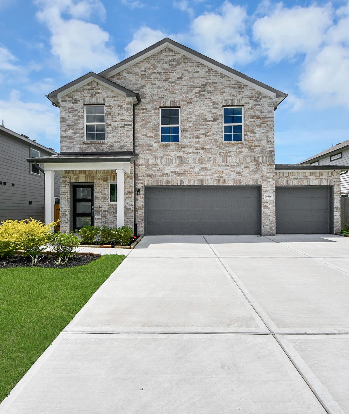 Brick home exterior at Hill & Dale Ranch in Splendora TX with covered porch, flagpoles, flower beds, and stone walkway