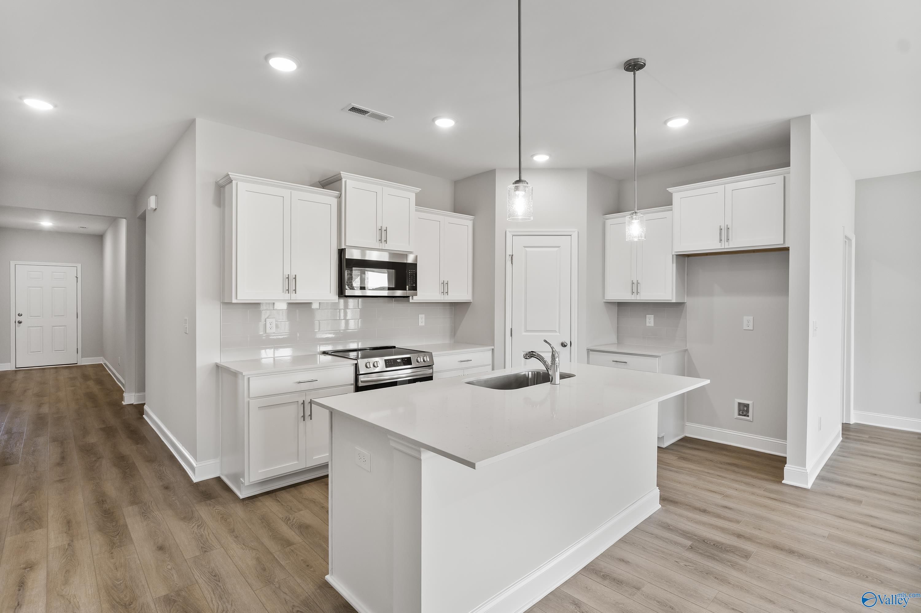 Modern white shaker kitchen with quartz island, stainless appliances, and open hallway in The Daphne 4-bedroom home, Hazel Green, AL