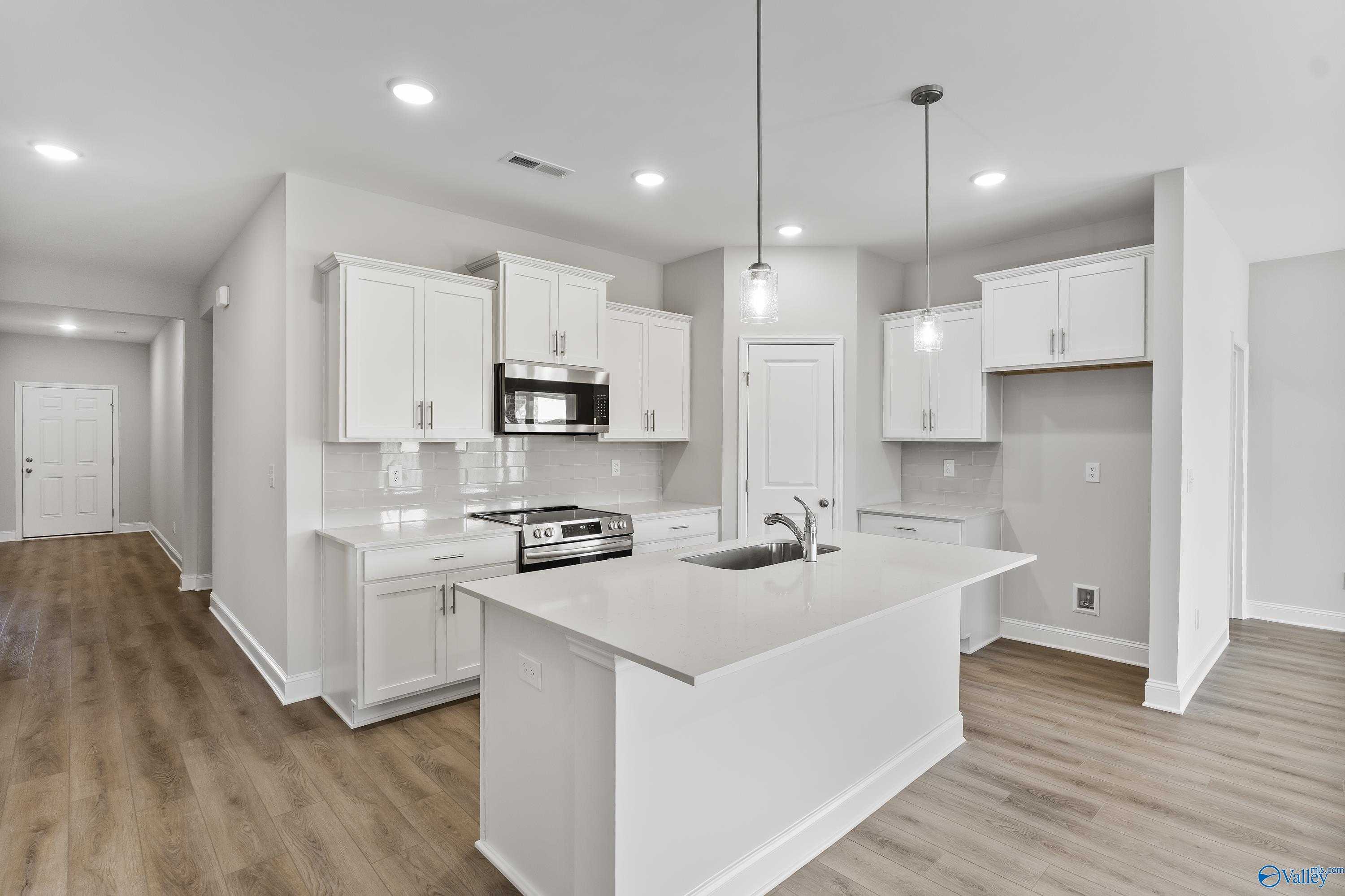 Modern white shaker kitchen with quartz island, stainless appliances, and open hallway in The Daphne 4-bedroom home, Hazel Green, AL