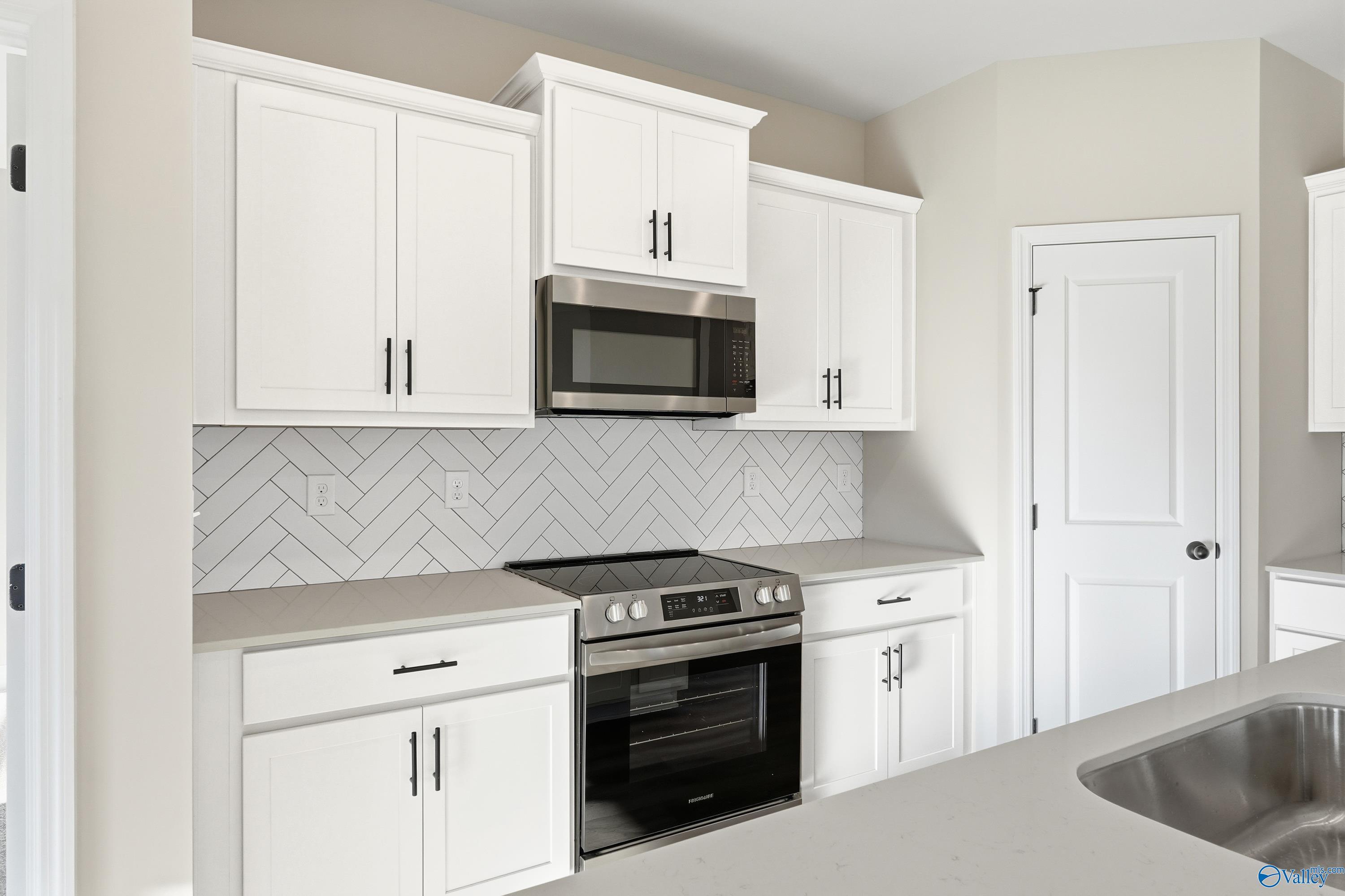 Modern kitchen featuring white shaker cabinets, stainless steel appliances, and herringbone tile backsplash in Davidson Homes The Franklin E, Hazel Green, Alabama