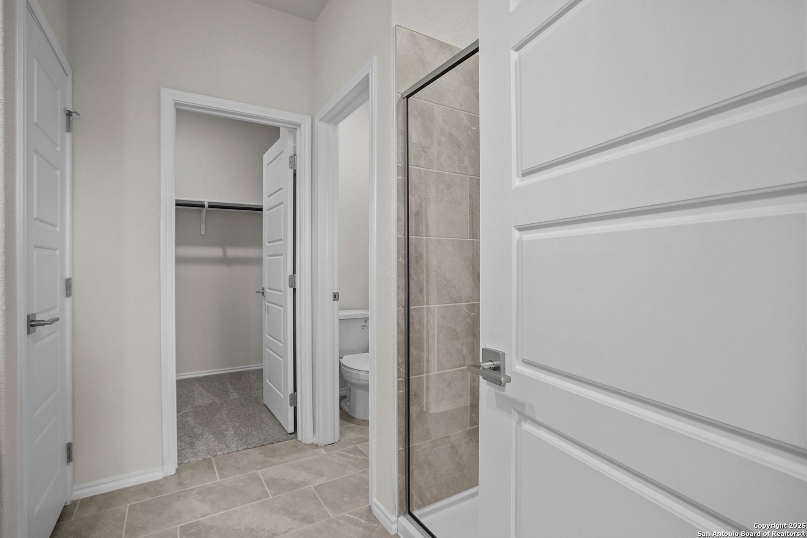 Modern master bathroom with glass shower, toilet, and adjacent walk-in closet in Davidson Homes The Asheville J, San Antonio, Texas