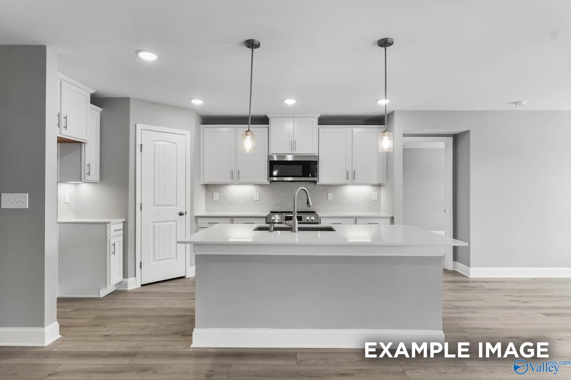 Modern white kitchen with large island sink, stainless appliances, and pendant lights in The Everett B floor plan, Toney, Alabama