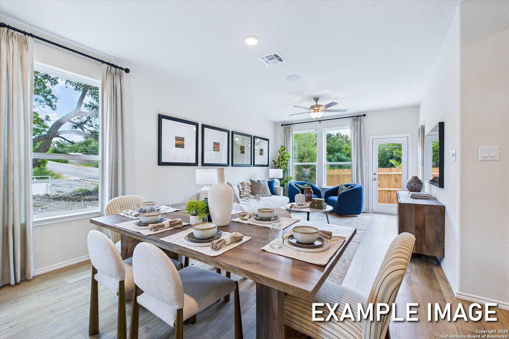 Spacious dining room with wooden table, white chairs, and large windows adjacent to living area with blue sofa in The Gillian B home, San Antonio