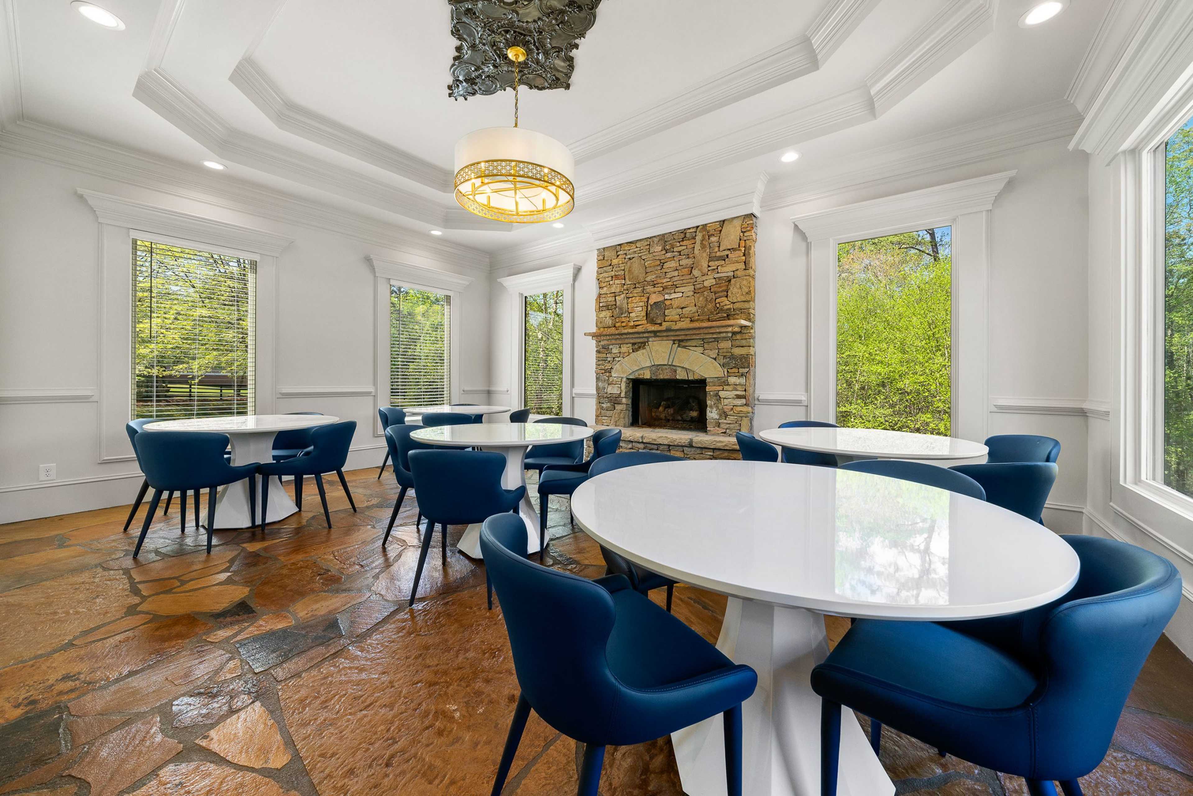 Cozy clubroom at Riverwood in Dallas Georgia featuring stone fireplace, round white tables, blue chairs, and large windows