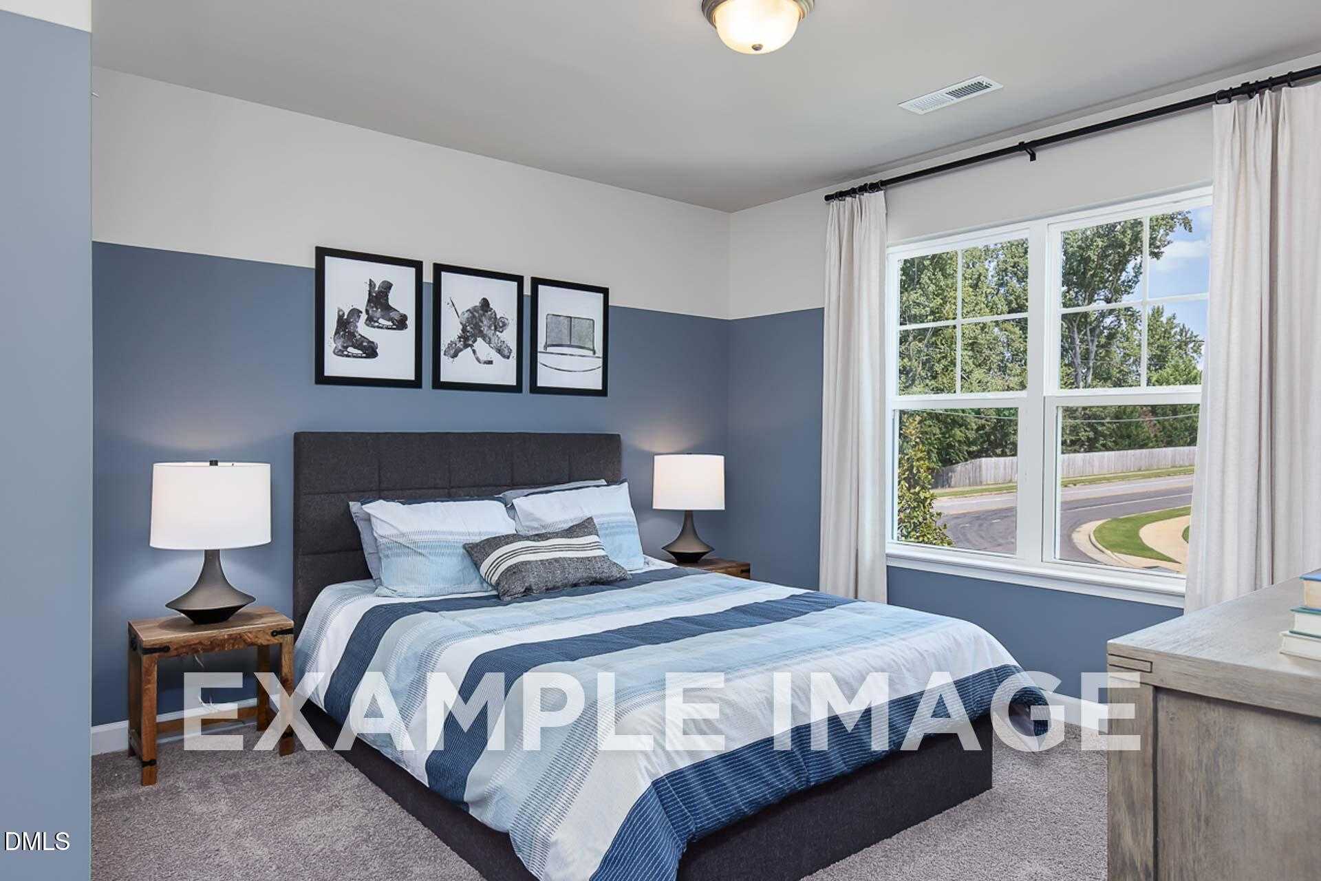 Cozy secondary bedroom with blue accent wall, striped bedding on platform bed, bedside lamps, and large window view in Davidson Homes The Ash B, Lillington, NC