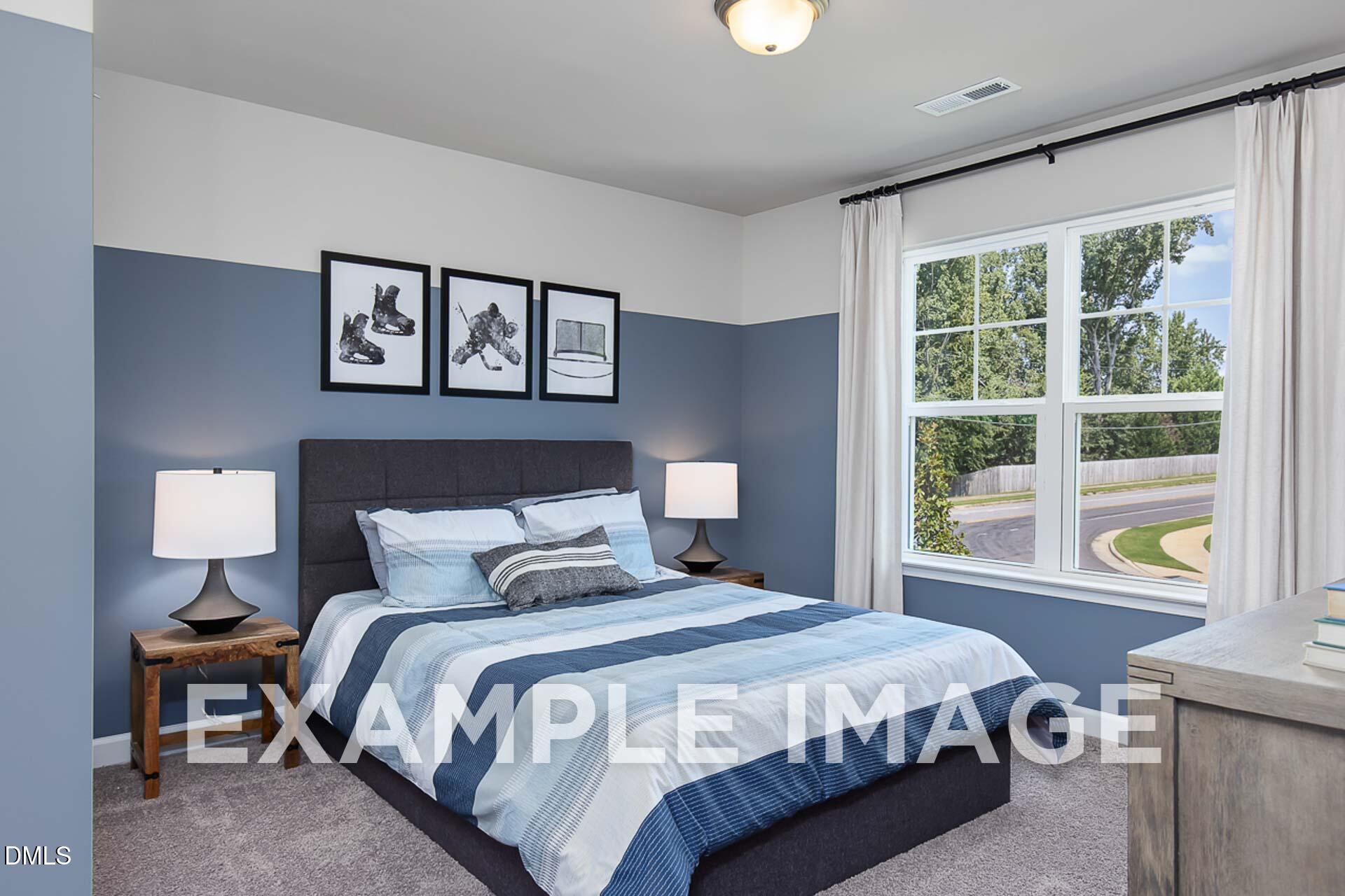 Cozy secondary bedroom featuring blue accent wall, striped bedding, bedside lamps, and window view in Davidson Homes The Ash B, Lillington, NC