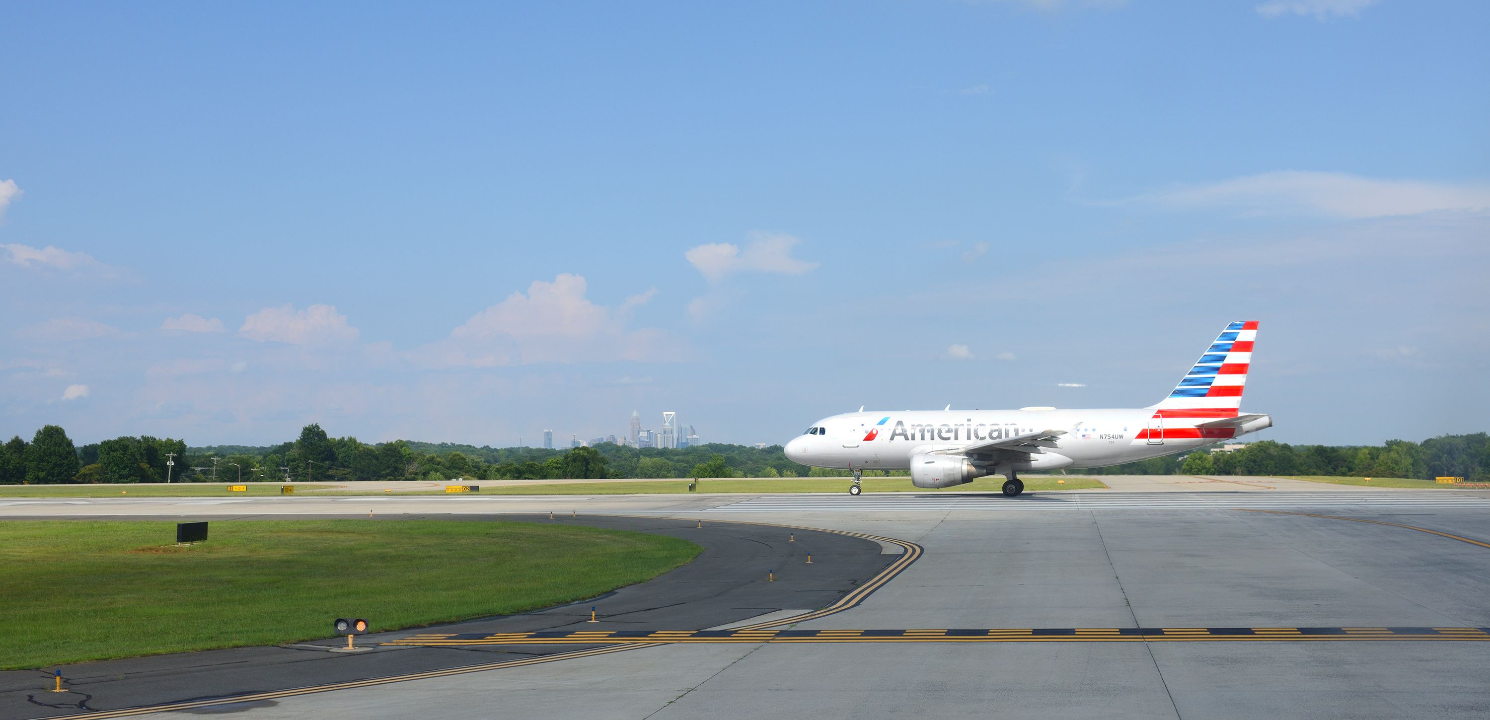 American Airlines jet taxiing at Charlotte Douglas International Airport with the Charlotte, NC skyline in the distance.