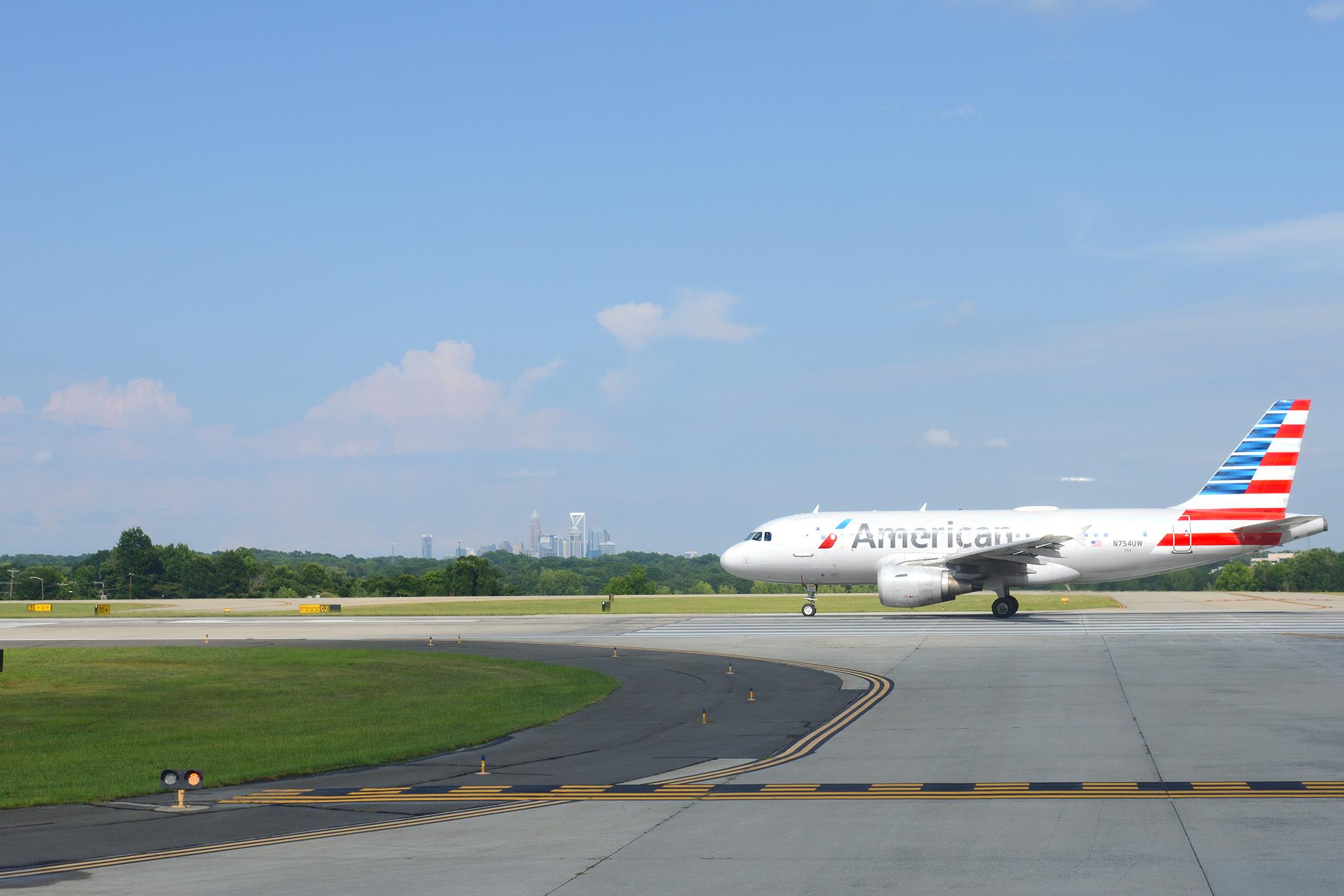 American Airlines jet taxiing at Charlotte Douglas International Airport with the Charlotte, NC skyline in the distance.