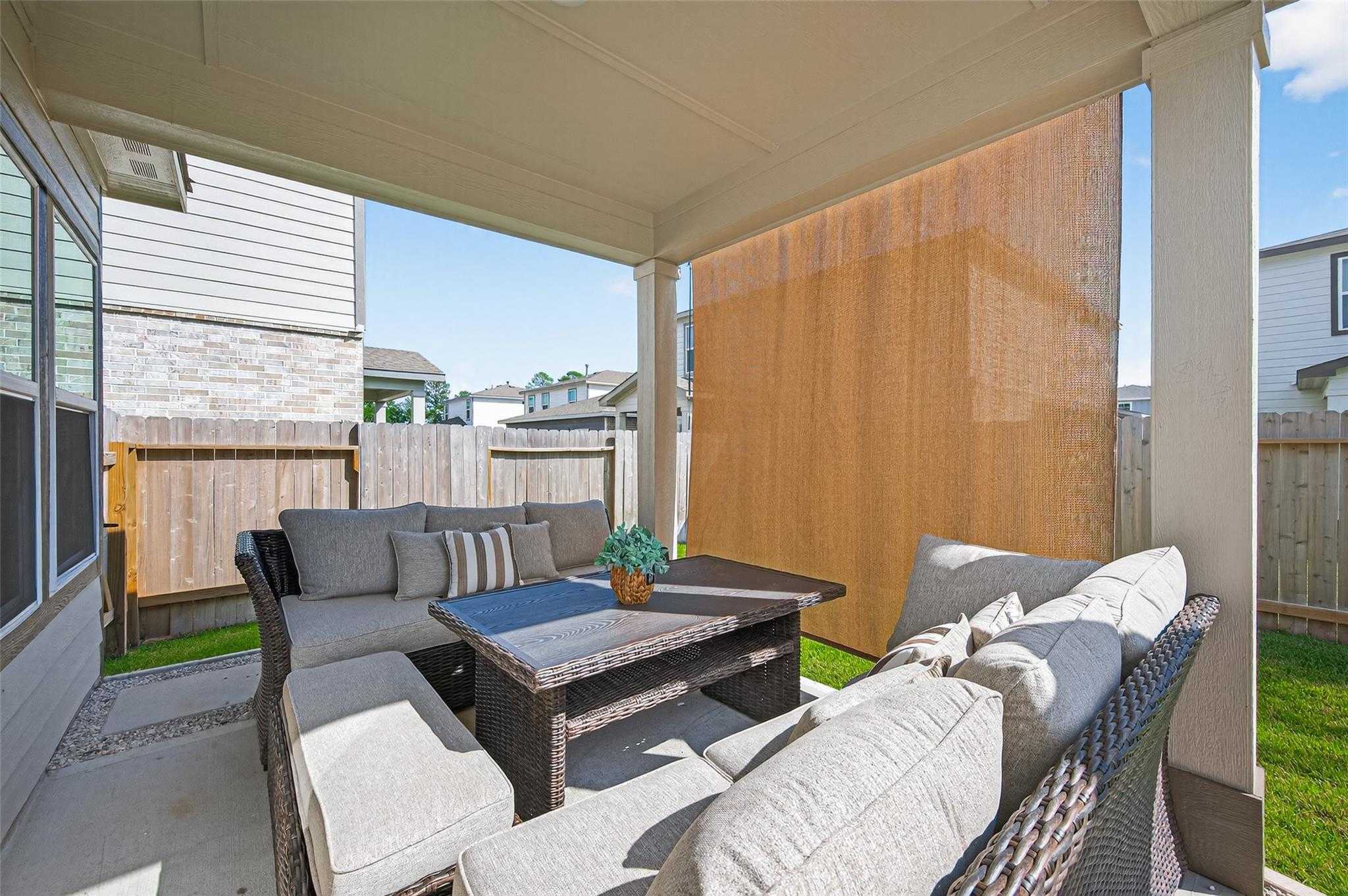 Cozy covered patio with gray sectional sofa, coffee table, and privacy screens overlooking grassy backyard in Davidson Homes The Brazos E, Magnolia, Texas