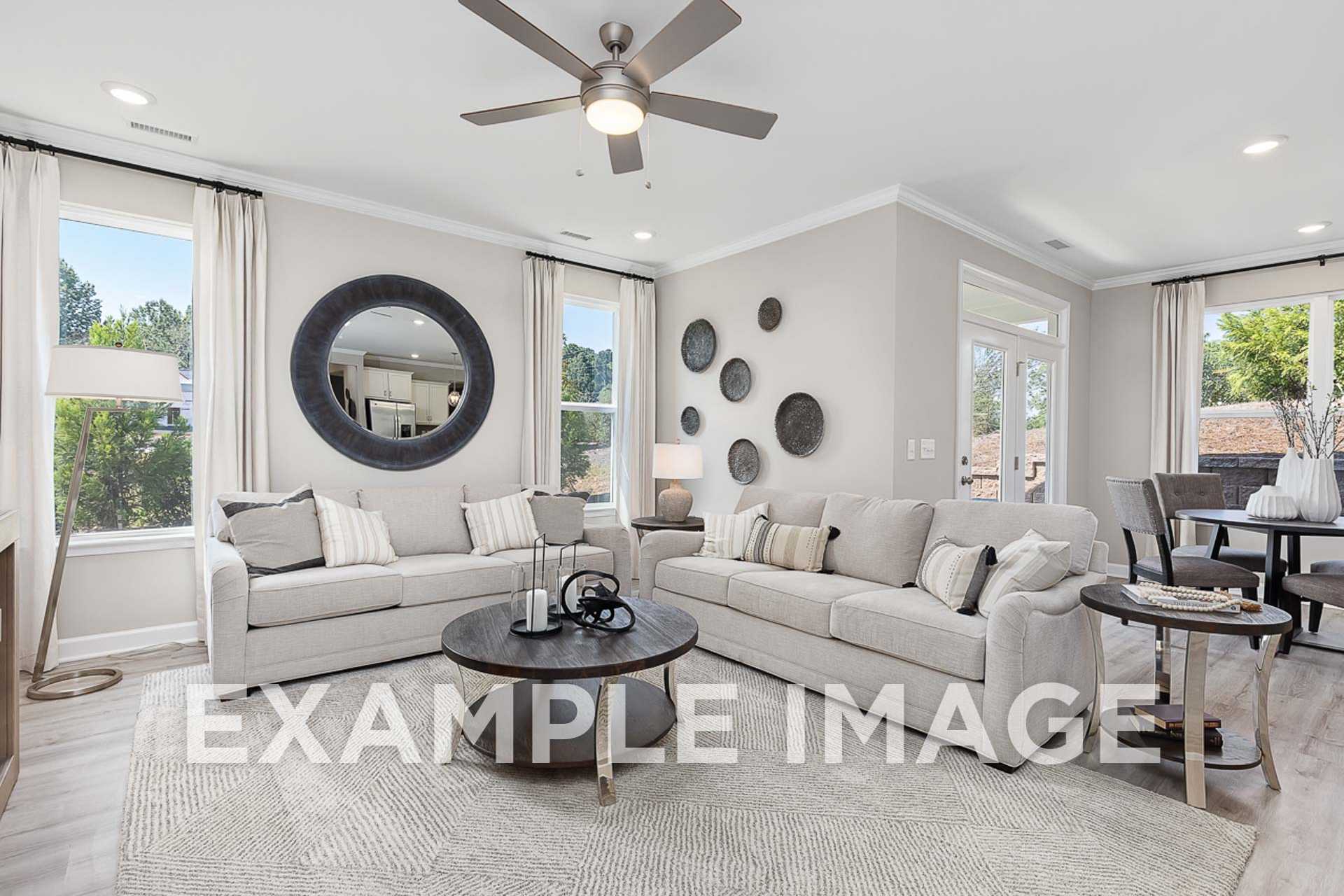 Spacious living room in The Ash E by Davidson Homes featuring gray L-shaped sofa, round coffee table, and large sunny windows