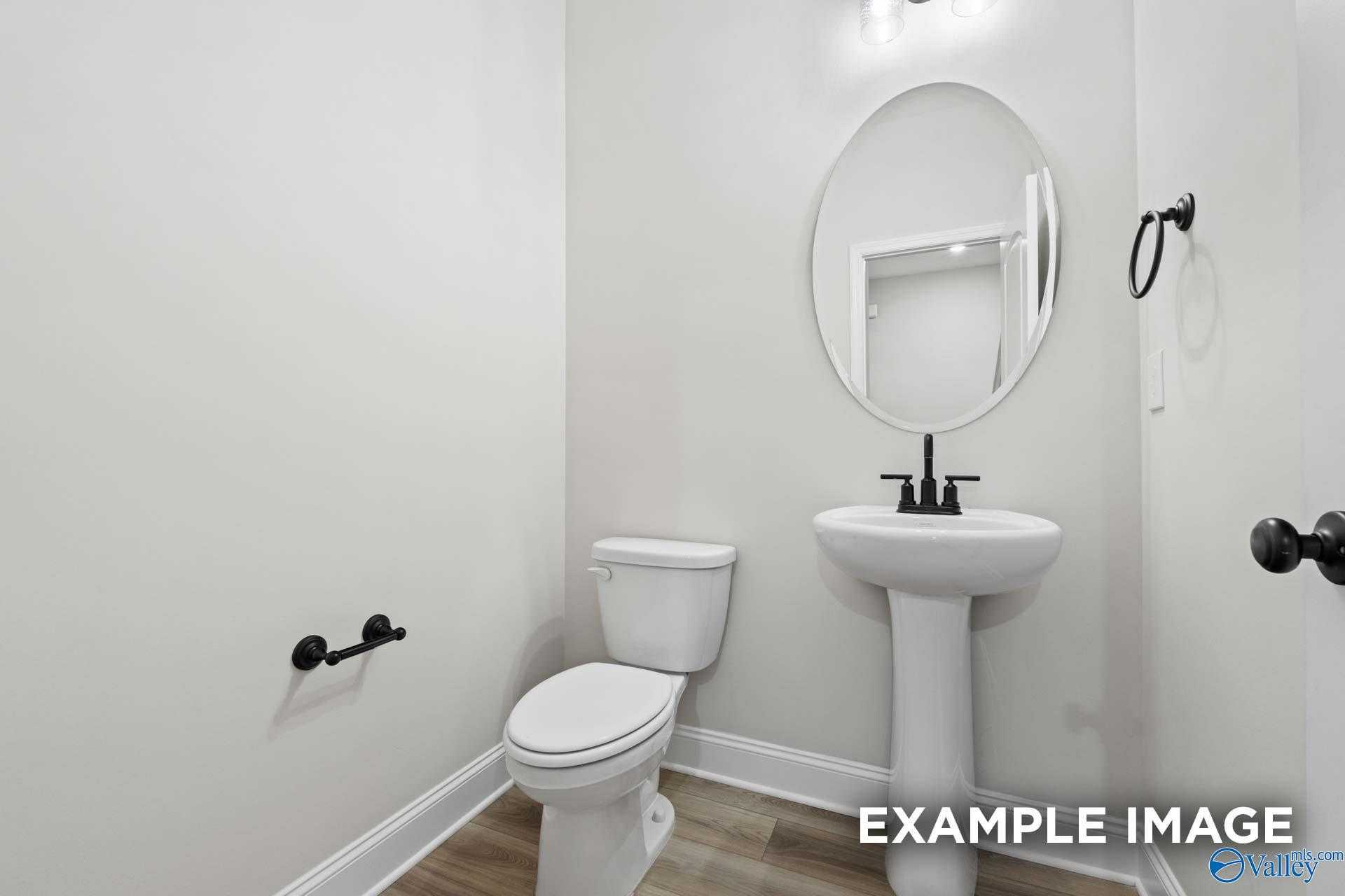Elegant powder room featuring pedestal sink, round mirror, and black fixtures in Davidson Homes The Camden D, Huntsville, Alabama
