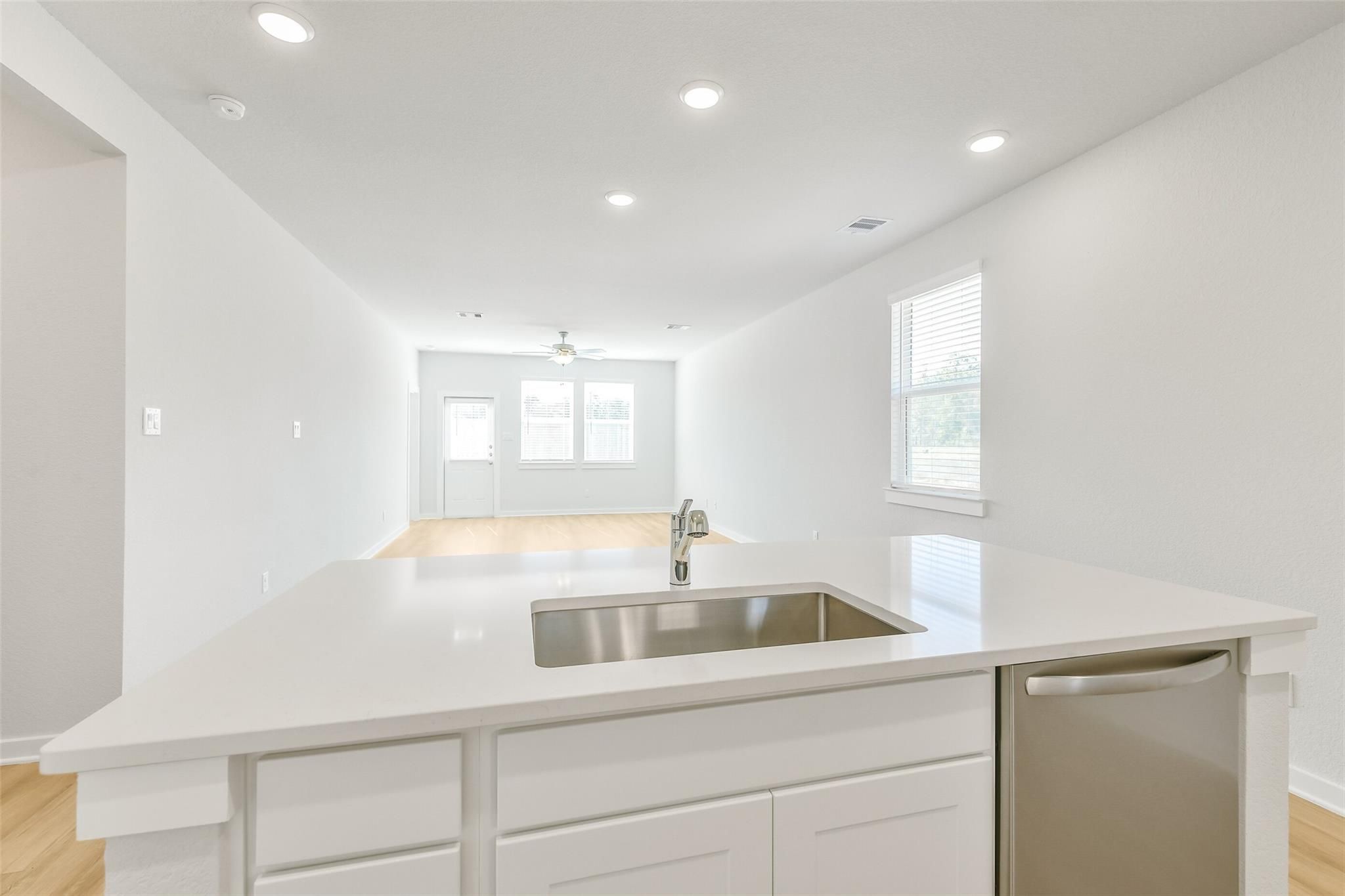 Modern white kitchen island with stainless steel sink and dishwasher in open-concept living area of Davidson Homes The San Marcos E, Cleveland, Texas