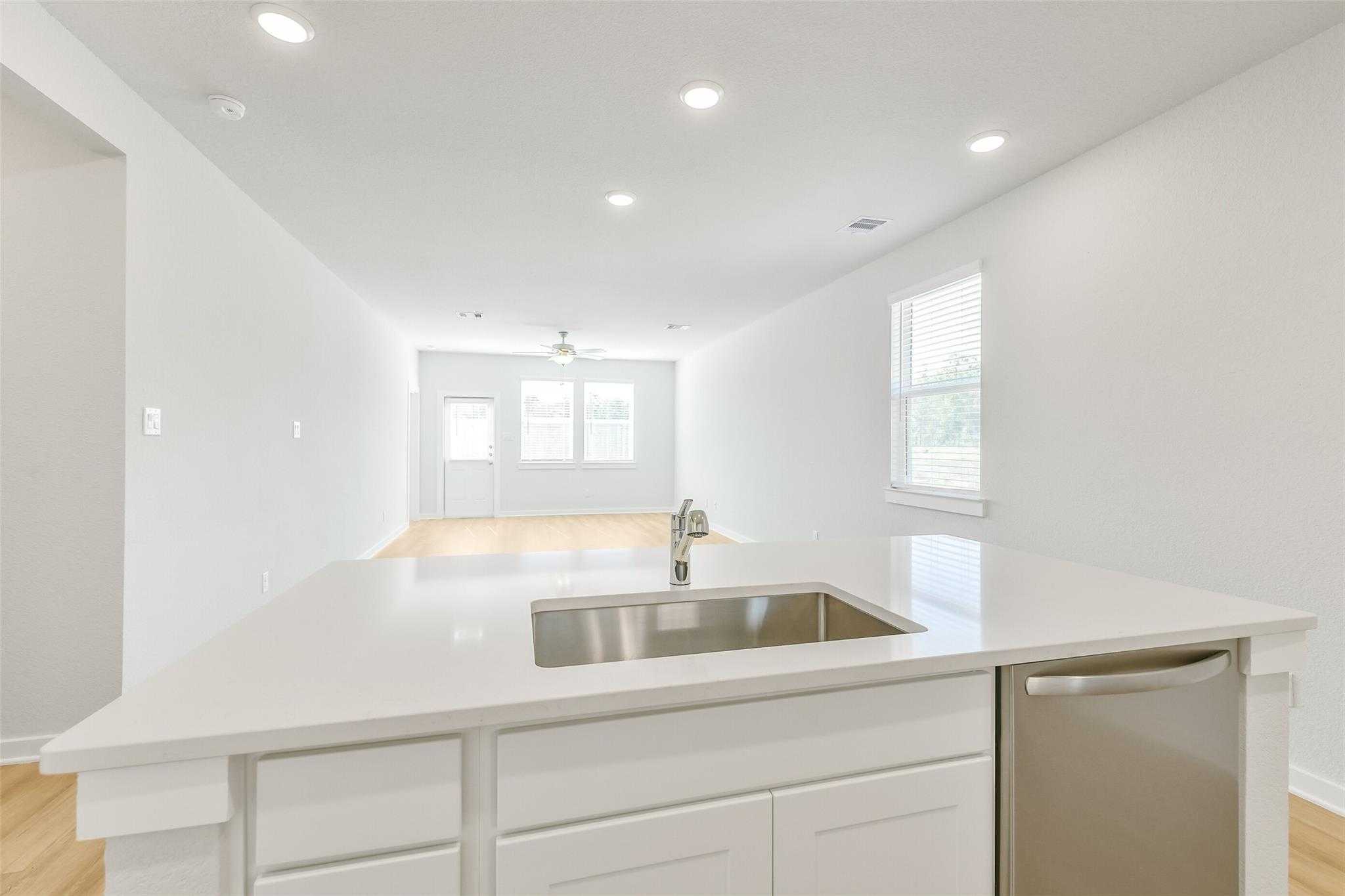 Modern white kitchen island with stainless steel sink and dishwasher in open-concept living area of Davidson Homes The San Marcos E, Cleveland, Texas