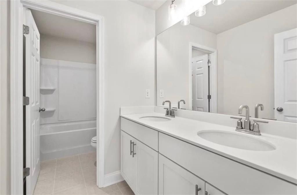Modern bathroom with double vanity and tub-shower combo in The Ash C floor plan at Wehunt Meadows, Hoschton, Georgia.