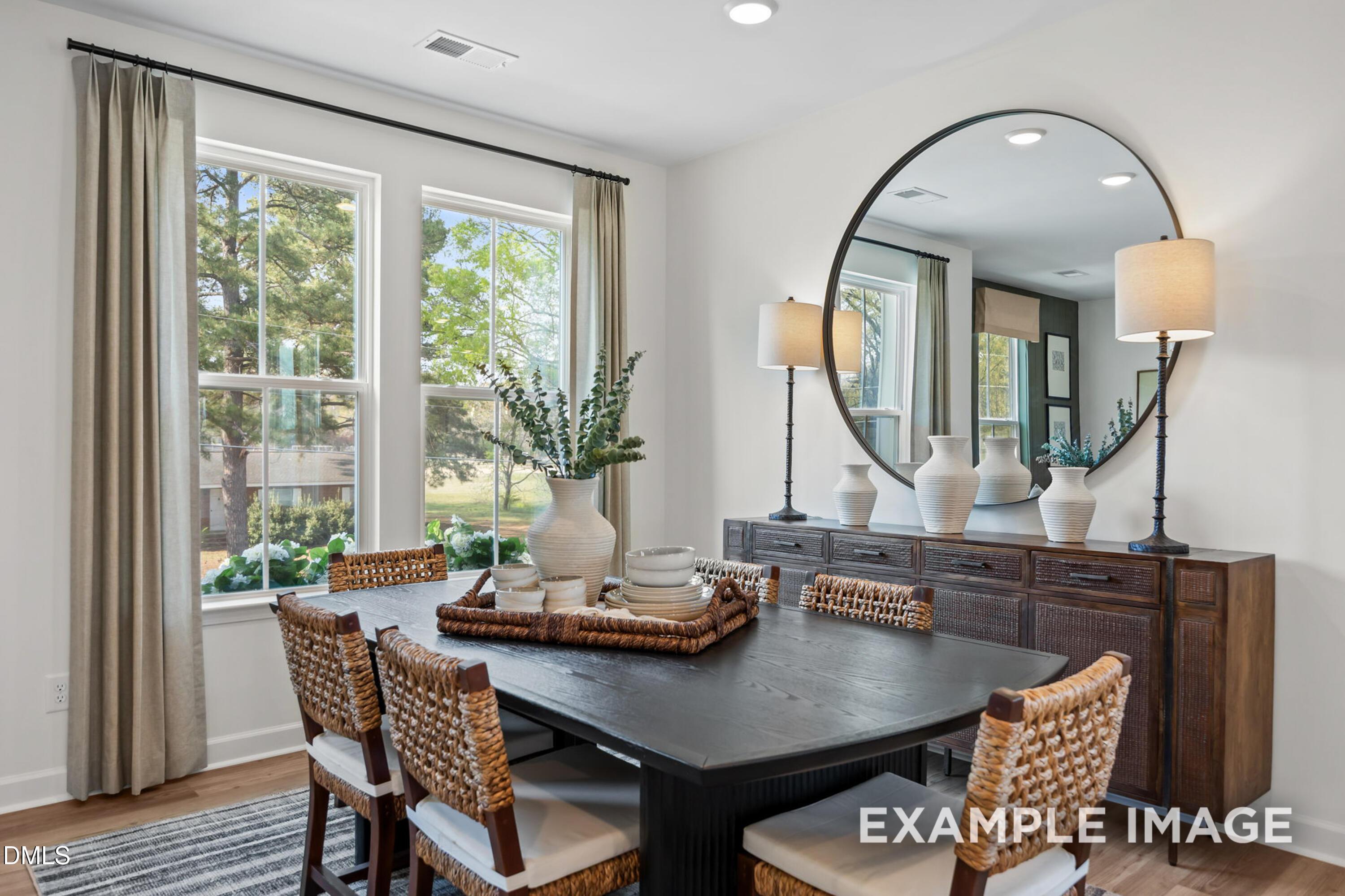 Elegant dining room featuring black rectangular table, wicker chairs, large round mirror, and window views in Davidson Homes The Mitchell, Knightdale, NC
