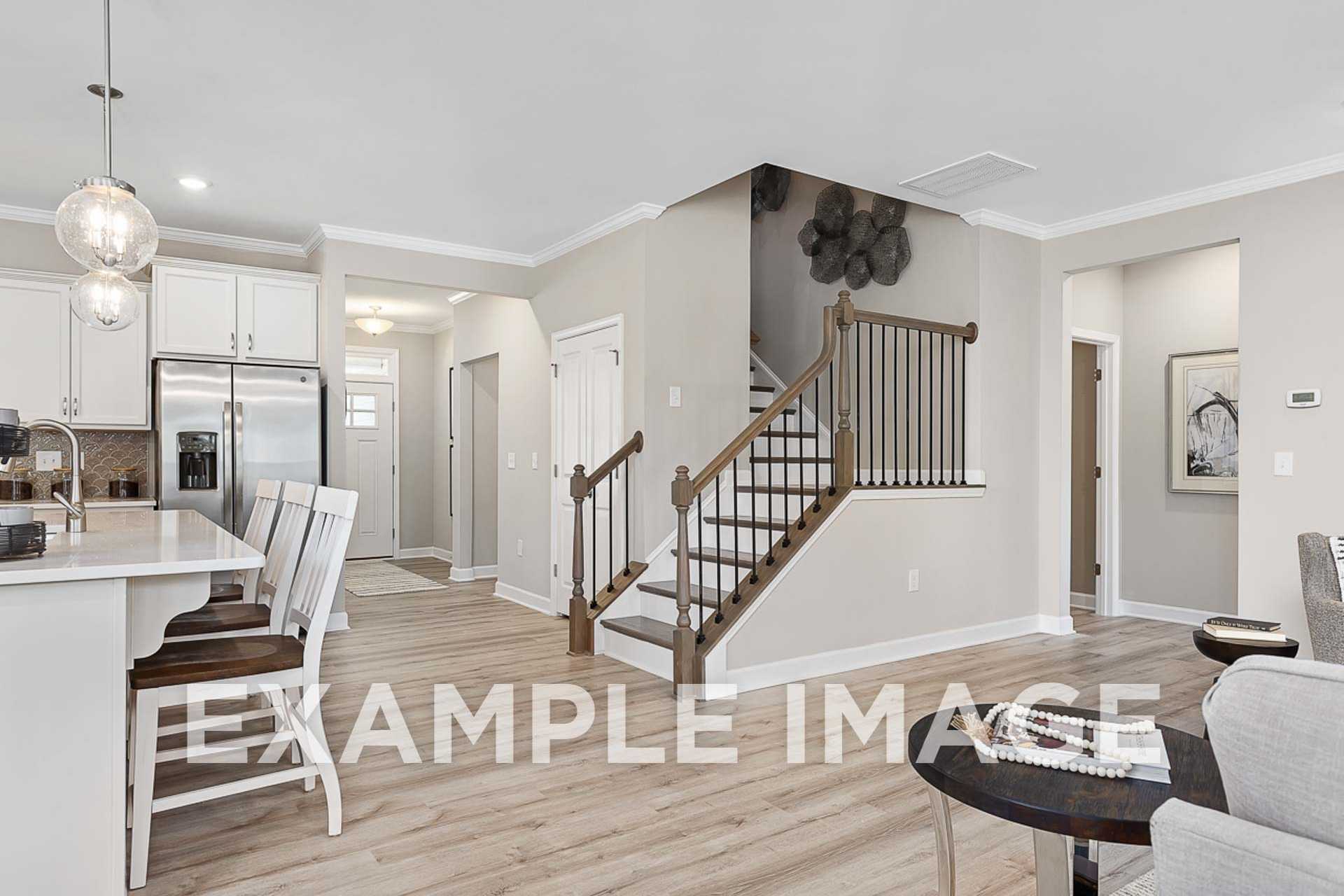 Spacious open-concept kitchen in The Ash E by Davidson Homes: white cabinets, large island, stainless appliances, wood staircase to upper suite