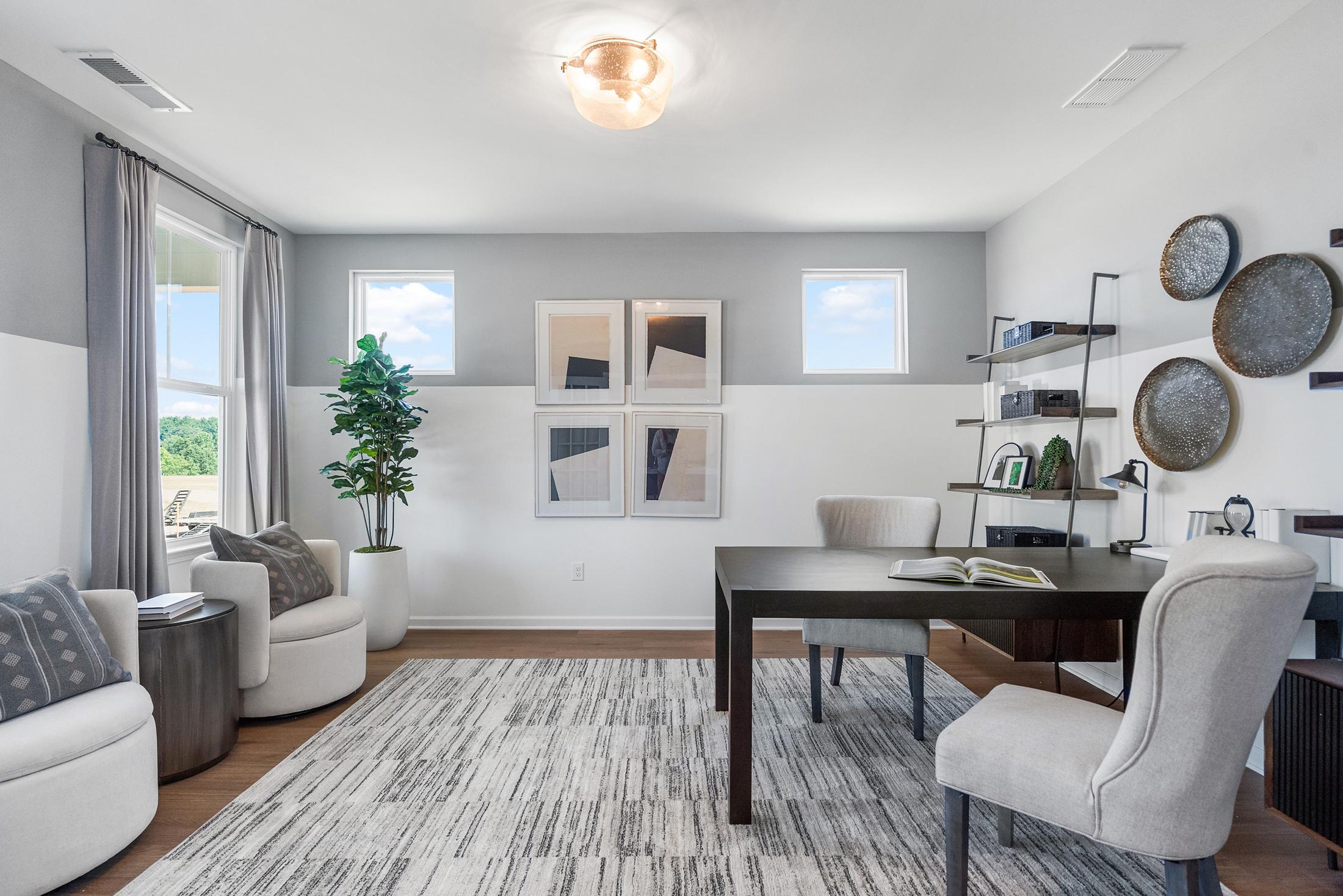 Modern home office in The Hickory B showcasing sleek wood desk, white armchairs, potted fiddle leaf fig, and abstract wall art