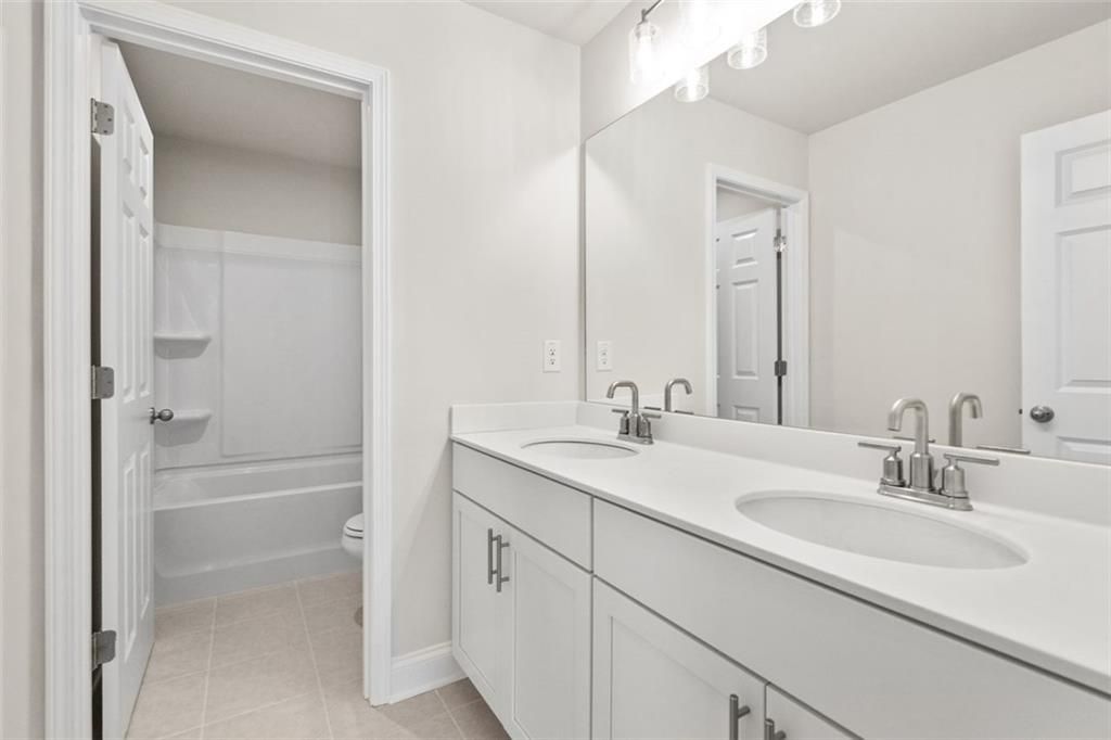 Bright bathroom with double white vanity, round sinks, large mirror, and tub in The Ash C at Wehunt Meadows, Hoschton, GA