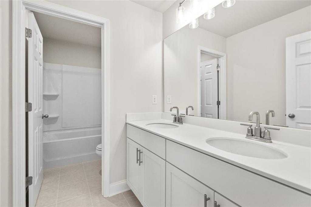 Bright bathroom with double white vanity, round sinks, large mirror, and tub in The Ash C at Wehunt Meadows, Hoschton, GA