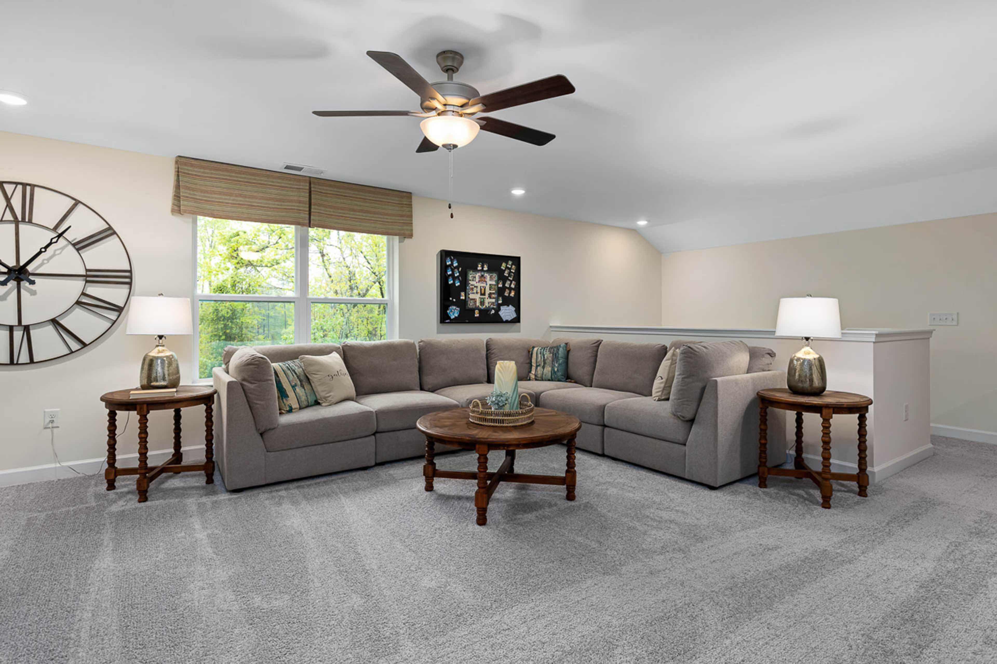 Cozy loft bonus room in Weatherford East home by Davidson Homes, Angier NC: gray L-shaped sectional sofa, ceiling fan, large wall clock