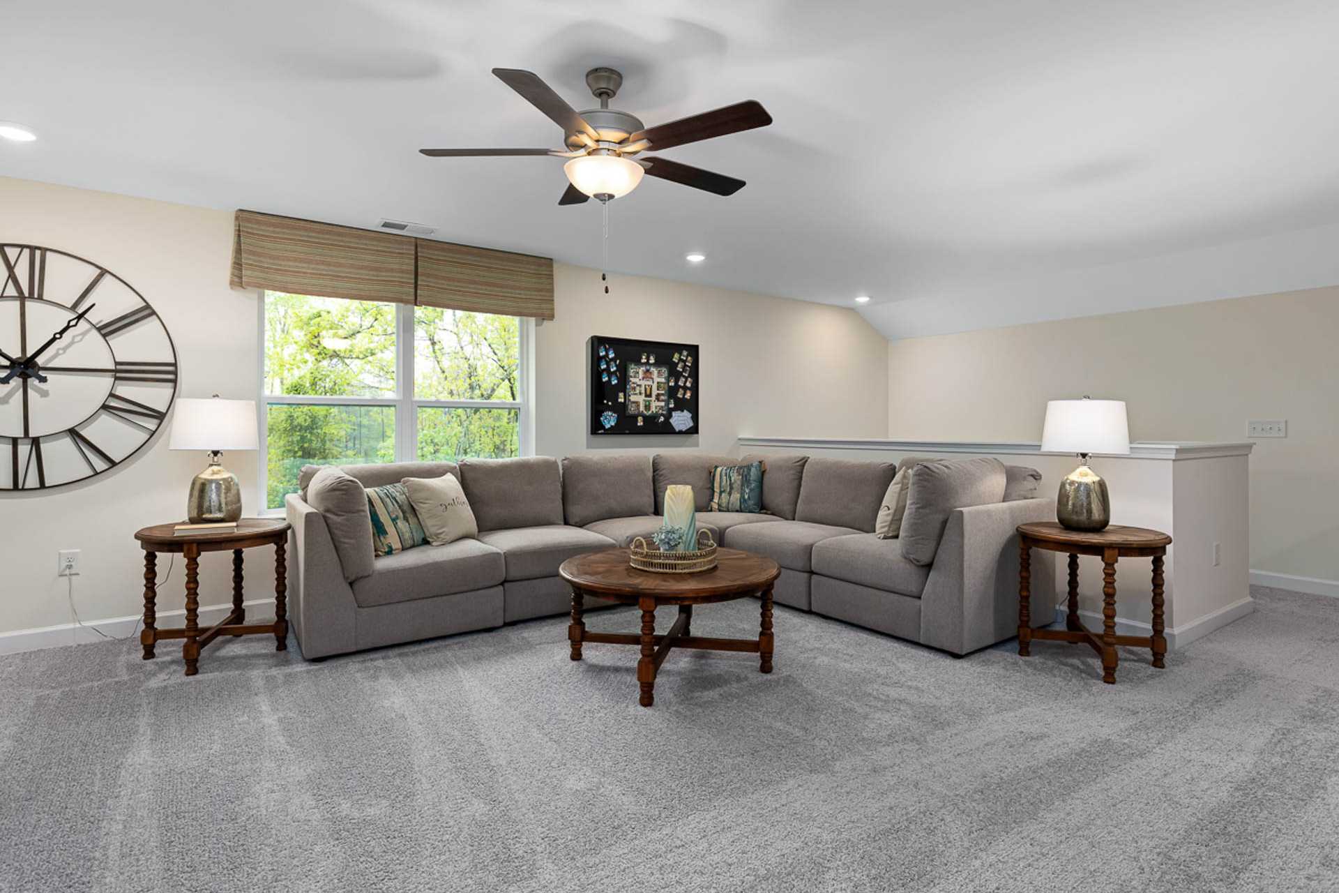 Cozy loft bonus room in Weatherford East home by Davidson Homes, Angier NC: gray L-shaped sectional sofa, ceiling fan, large wall clock