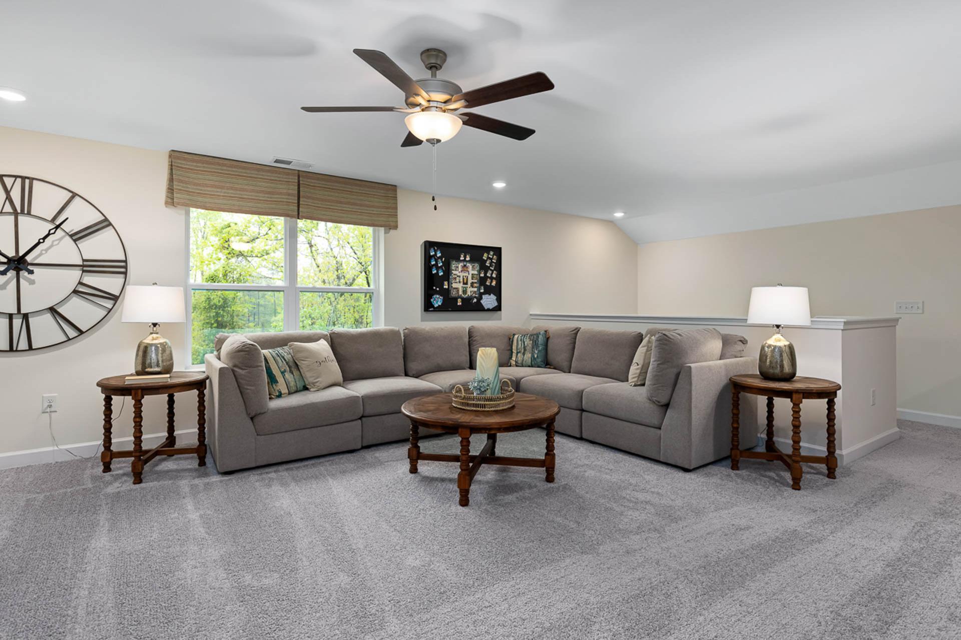 Cozy loft bonus room in Weatherford East home by Davidson Homes, Angier NC: gray L-shaped sectional sofa, ceiling fan, large wall clock