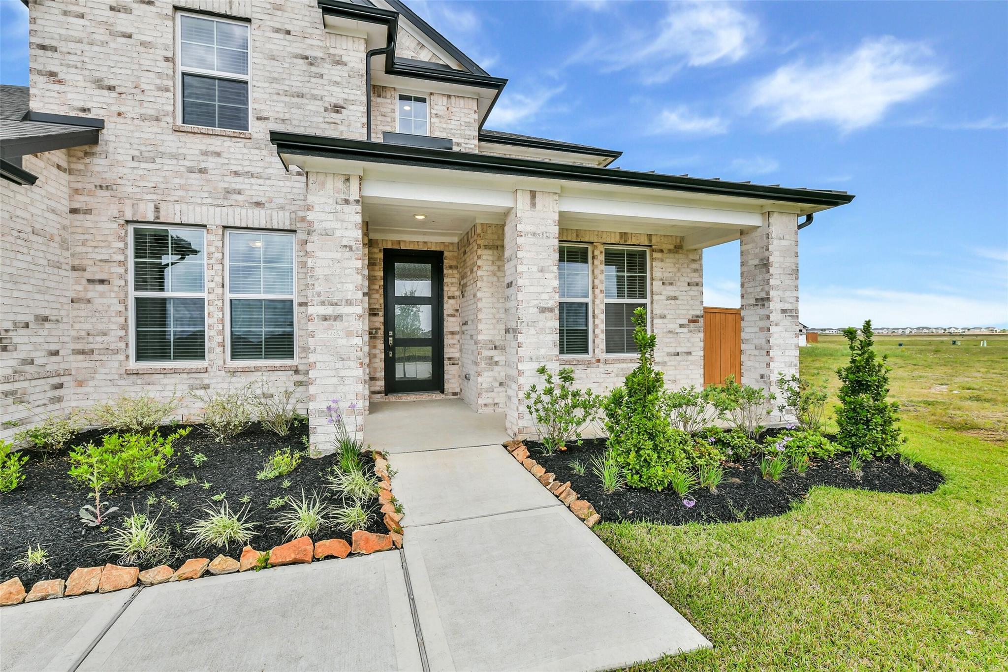 Two-story brick home with covered front porch, brick columns, glass door, and landscaped yard in Lago Mar, Texas City