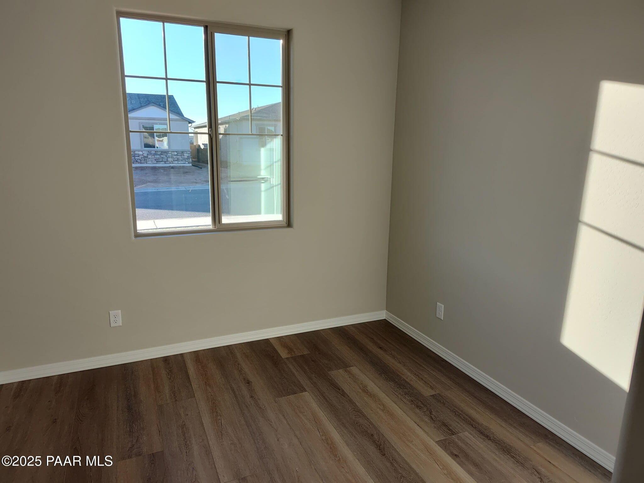 Bright secondary bedroom with beige walls, luxury vinyl plank flooring, and large window overlooking pool in 2-bed Davidson Homes Frontier A, Prescott Valley, AZ