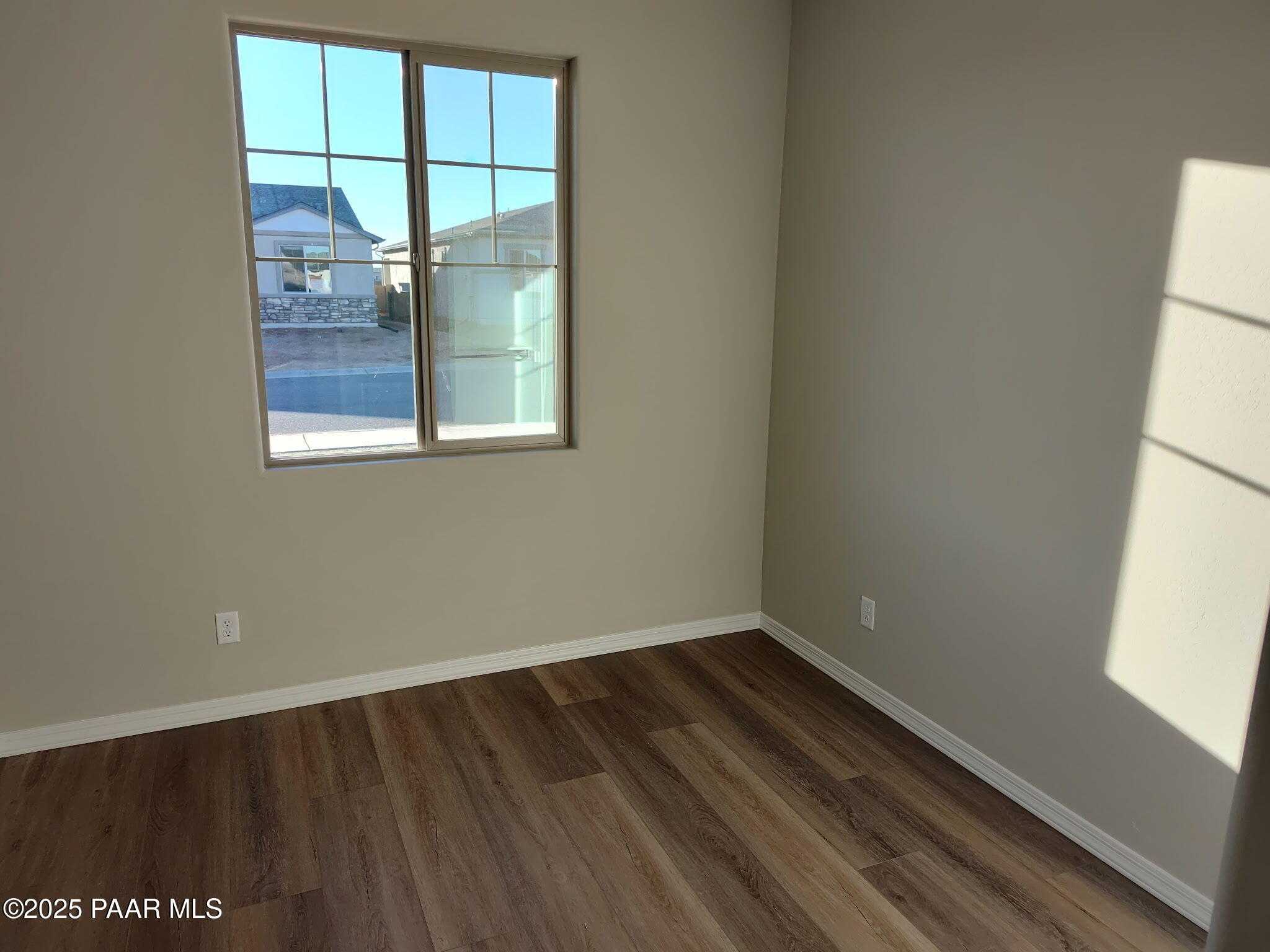 Bright secondary bedroom with beige walls, luxury vinyl plank flooring, and large window overlooking pool in 2-bed Davidson Homes Frontier A, Prescott Valley, AZ