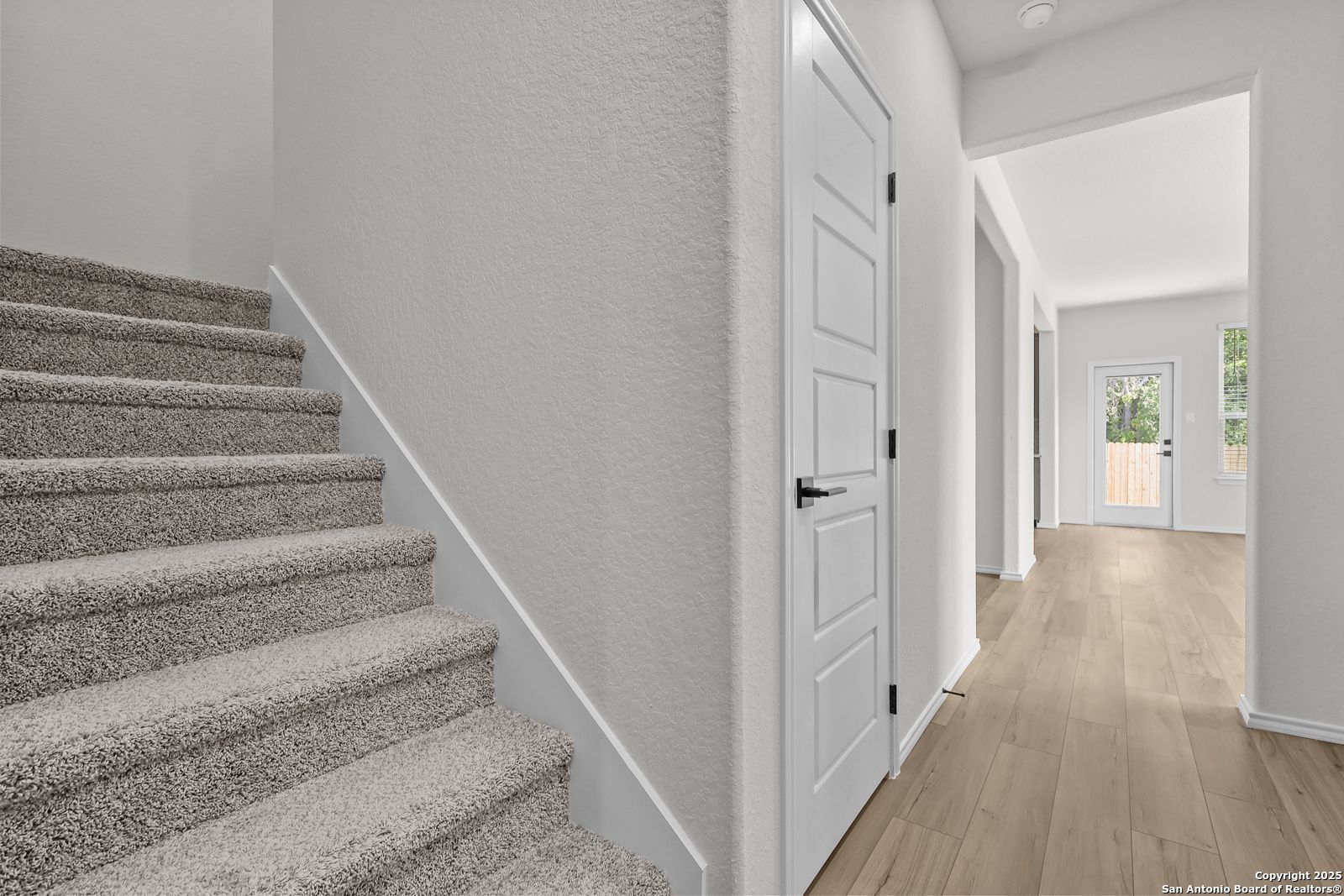 Carpeted staircase ascending to second floor beside open hallway with hardwood floors in The Florence C 2-story home, San Antonio
