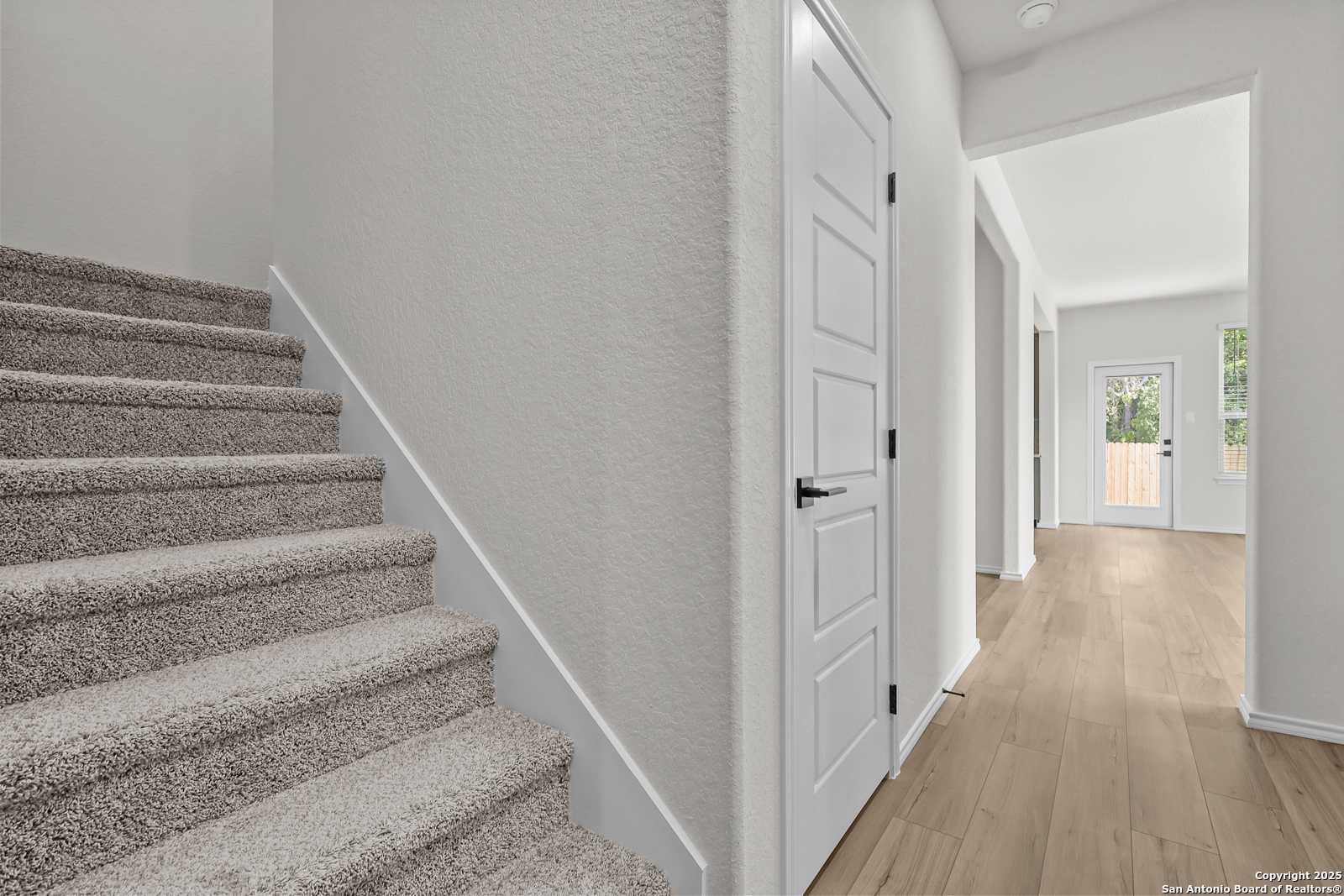 Carpeted staircase ascending to second floor beside open hallway with hardwood floors in The Florence C 2-story home, San Antonio